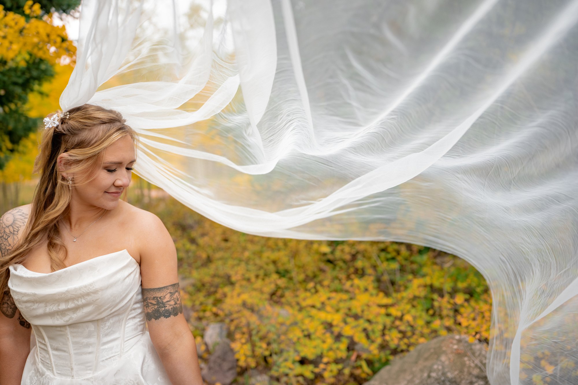 Bride looking over her shoulder with her veil billowing beside autumn foliage