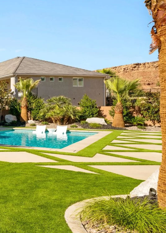 A backyard oasis showcasing bright artificial AGL Grass, elegant palm trees, and a crystal clear blue pool, ideal for enjoying sunny days outdoors.