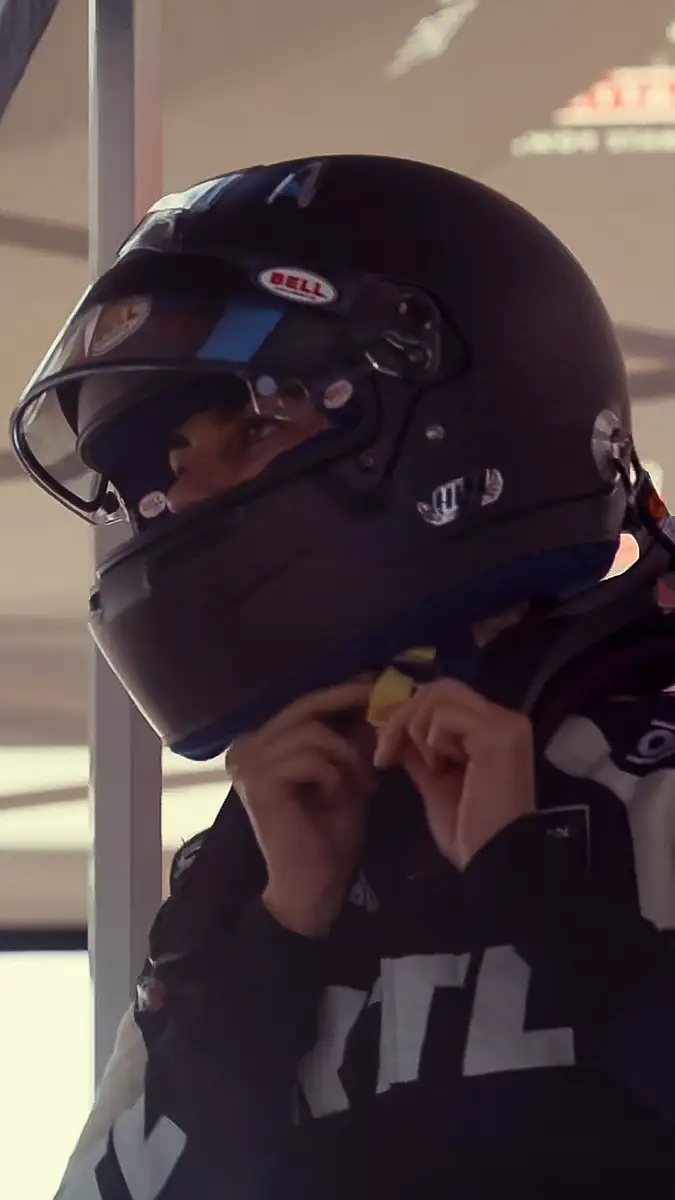 Emelia Hartford, in a racing suit, adjusting her helmet before the race.