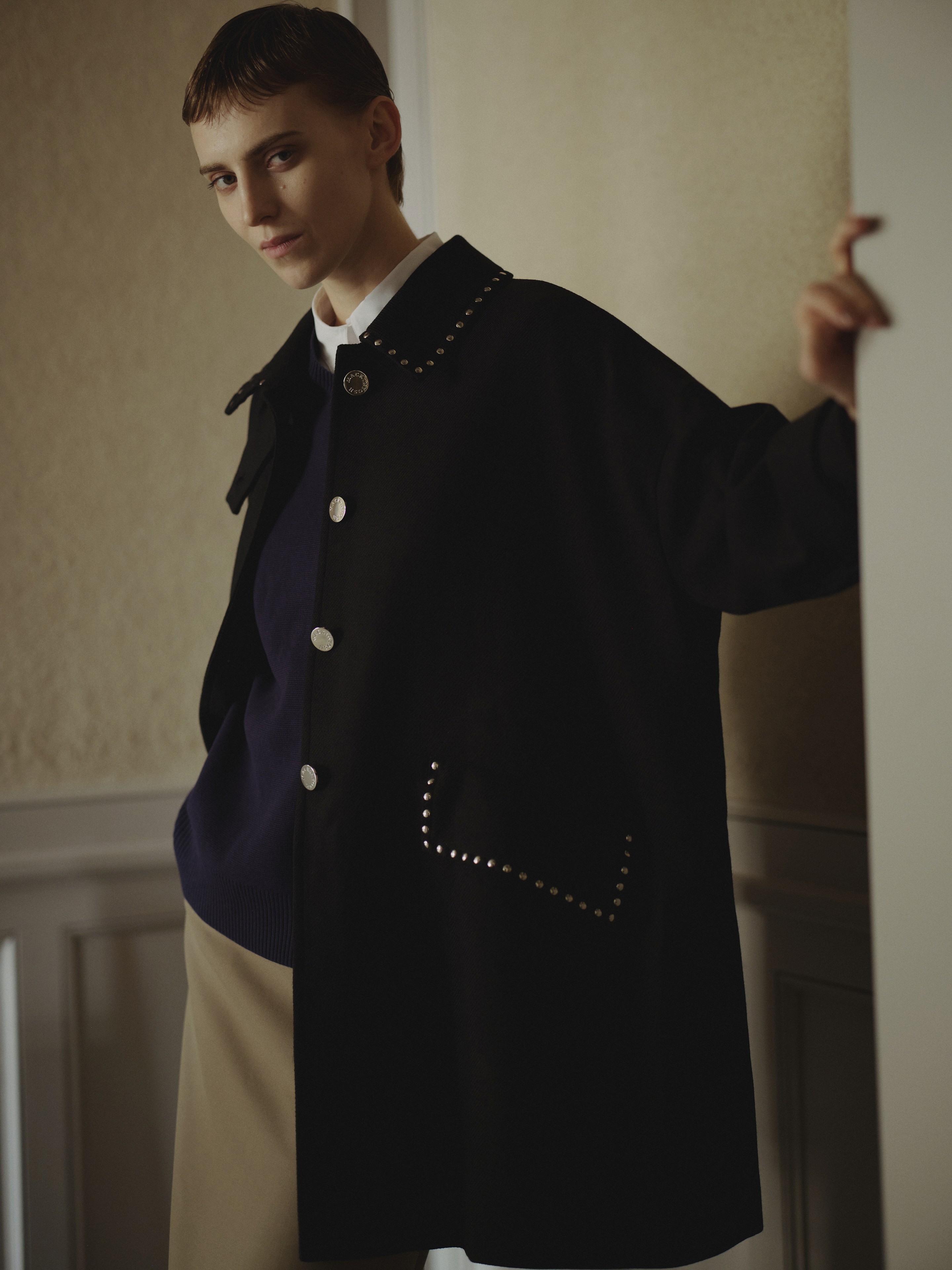 Une femme regarde l'objectif portant un manteau en laine noir,un pull et un pantalon beige