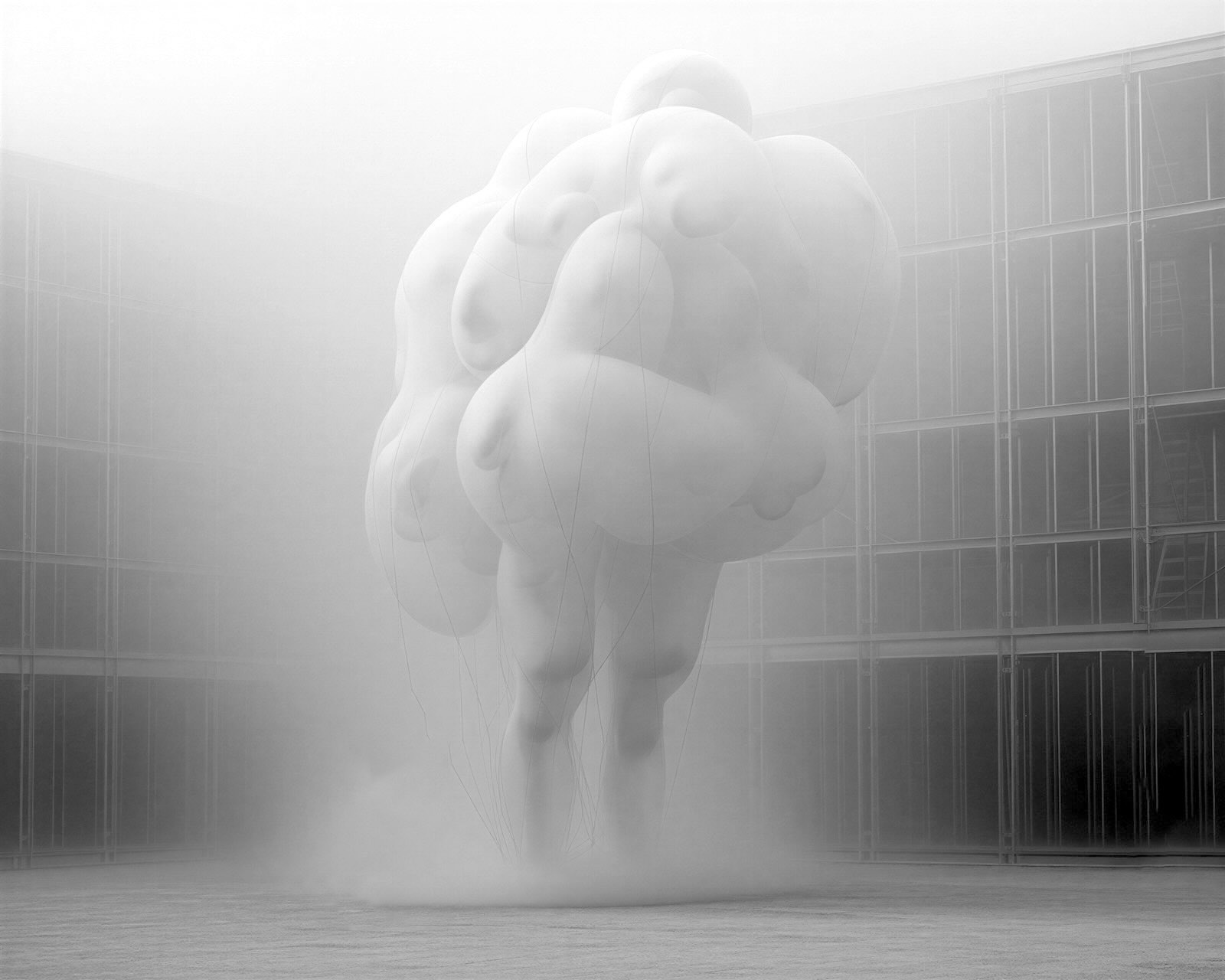Black-and-white image of a pale, blurred human figure appearing to float or leap in a misty modern interior.