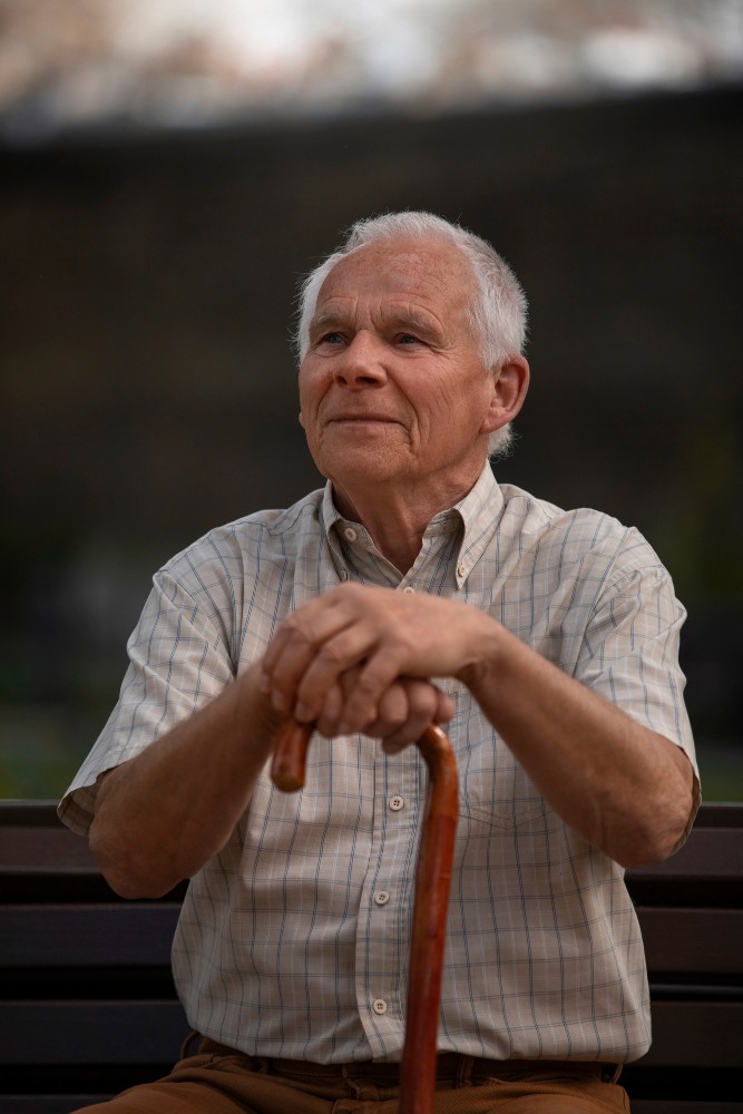 Senior man with white hair sitting outdoors, looking thoughtfully into the distance