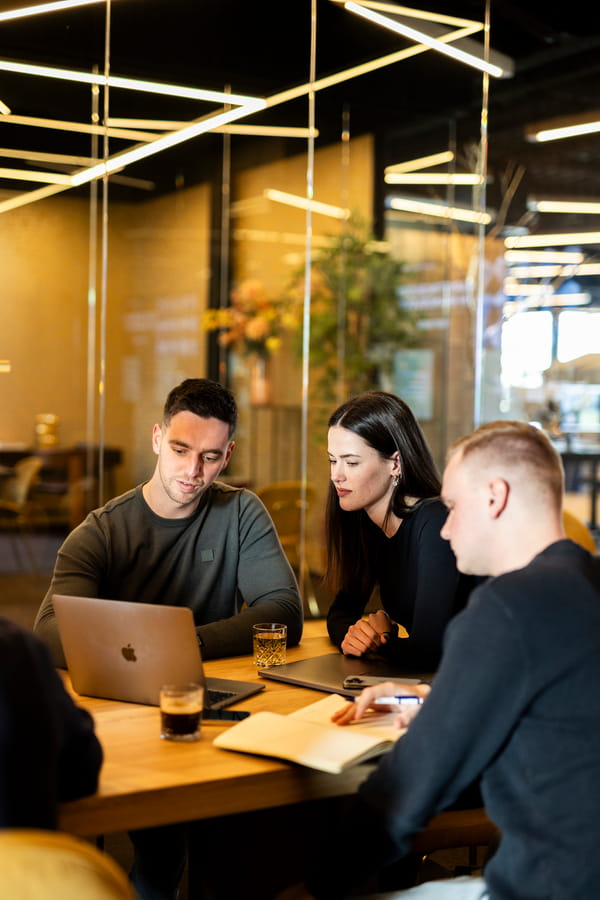 Three individuals gathered around a table, engaged in discussion while examining a laptop.