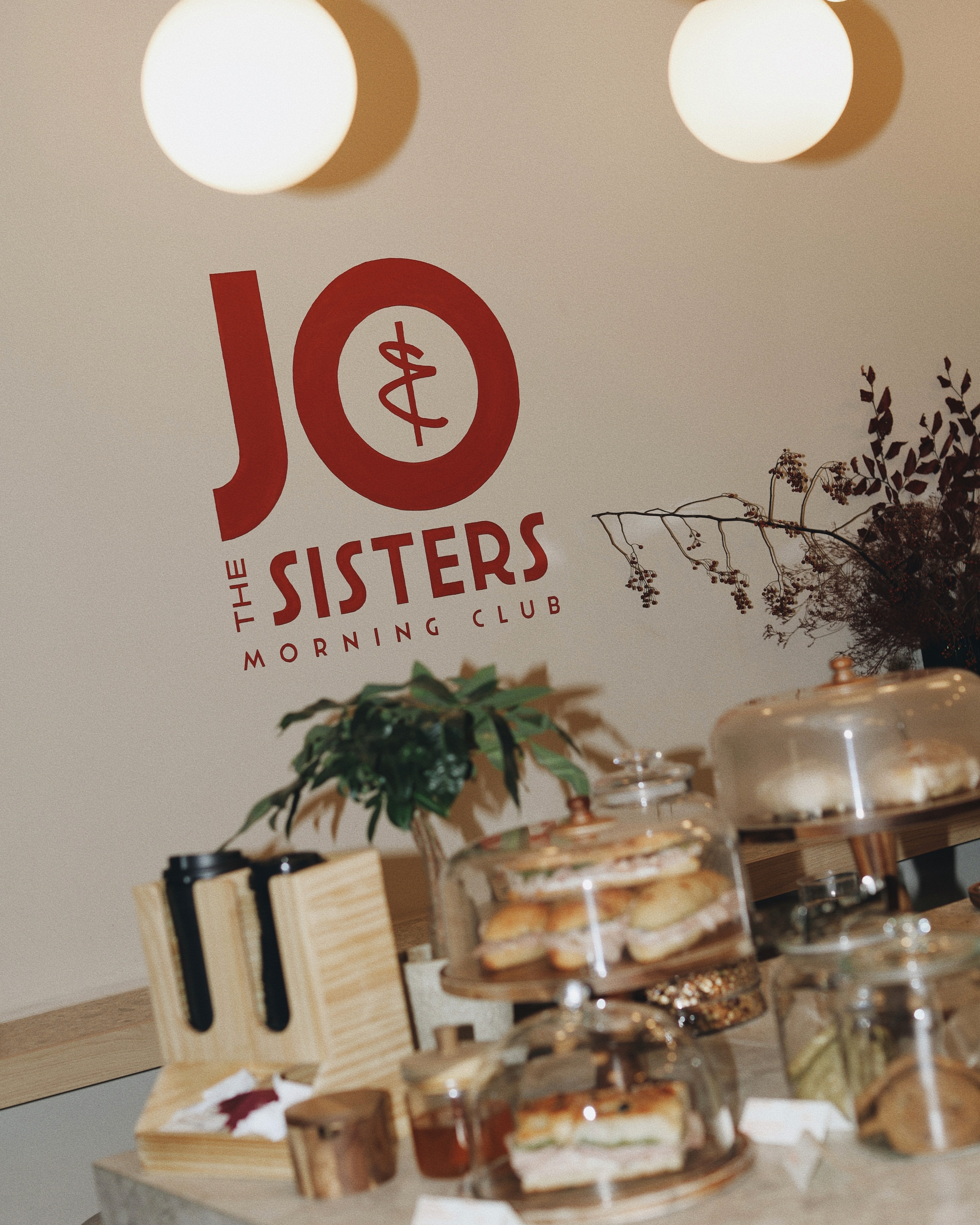 Jo & The Sisters Morning Club logo displayed above a breakfast counter with fresh pastries and sandwiches.