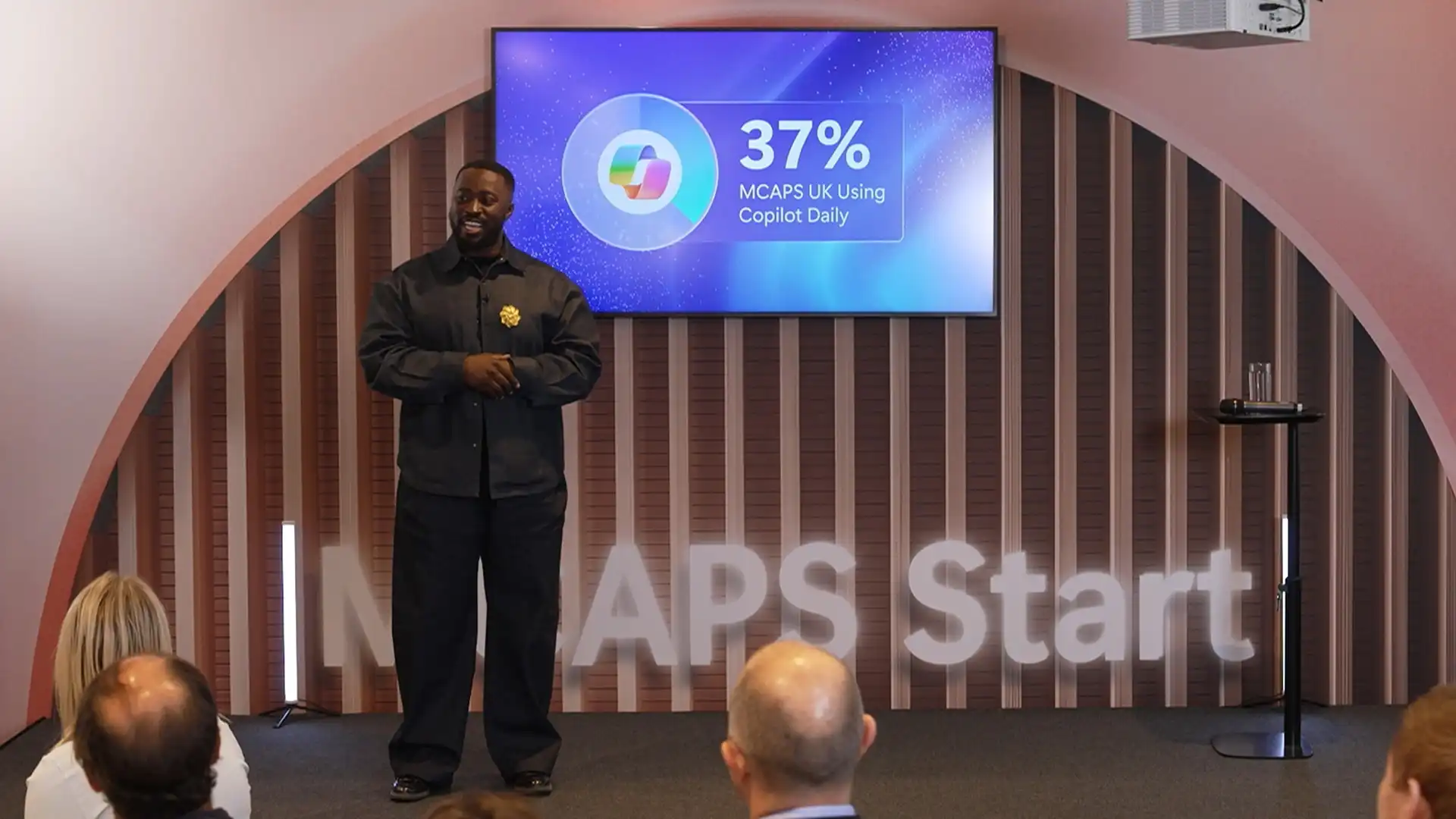 Presenter delivering a live Microsoft keynote on stage, with on-screen data visualisation highlighting daily use of Copilot.