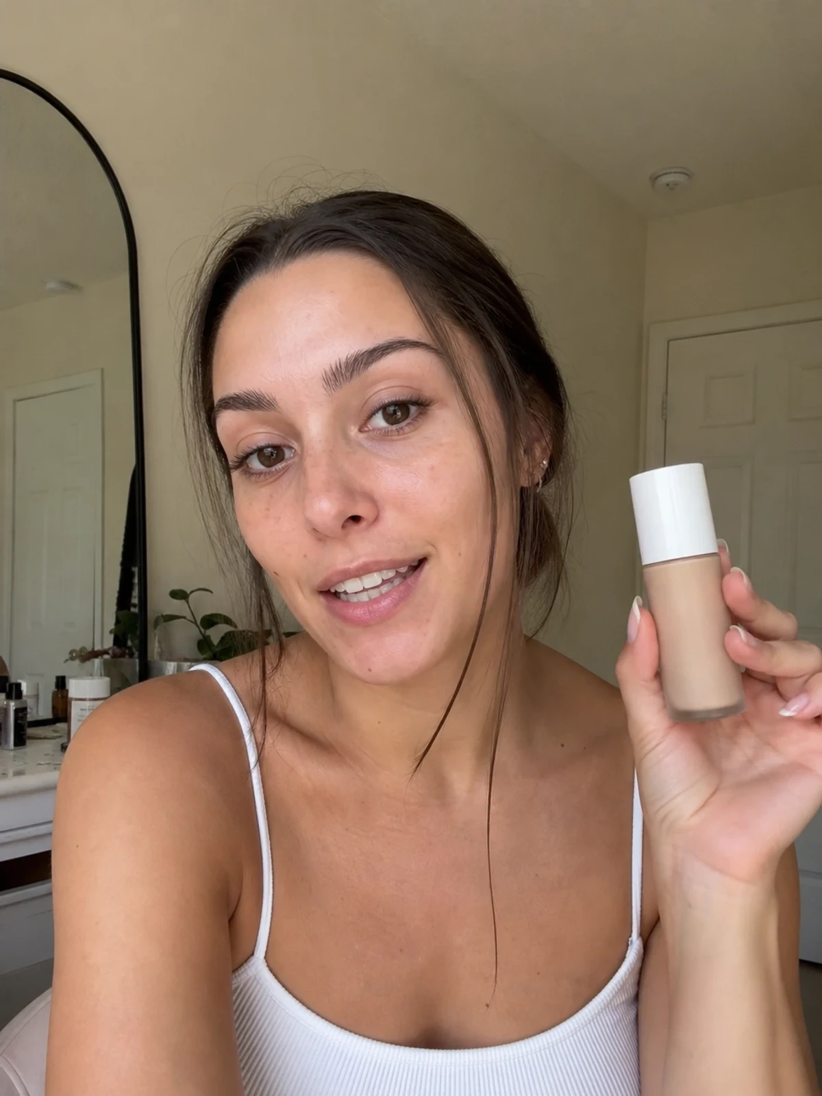 UGC creator at a bedroom vanity, holding a simple makeup product and talking to camera.