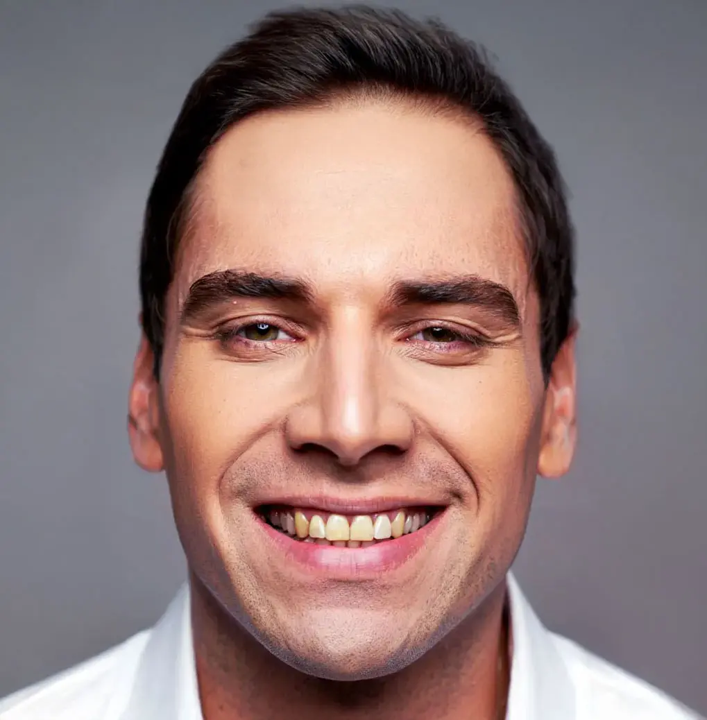Close up portrait of a man with dark hair and a wide smile, wearing a white collared shirt.
