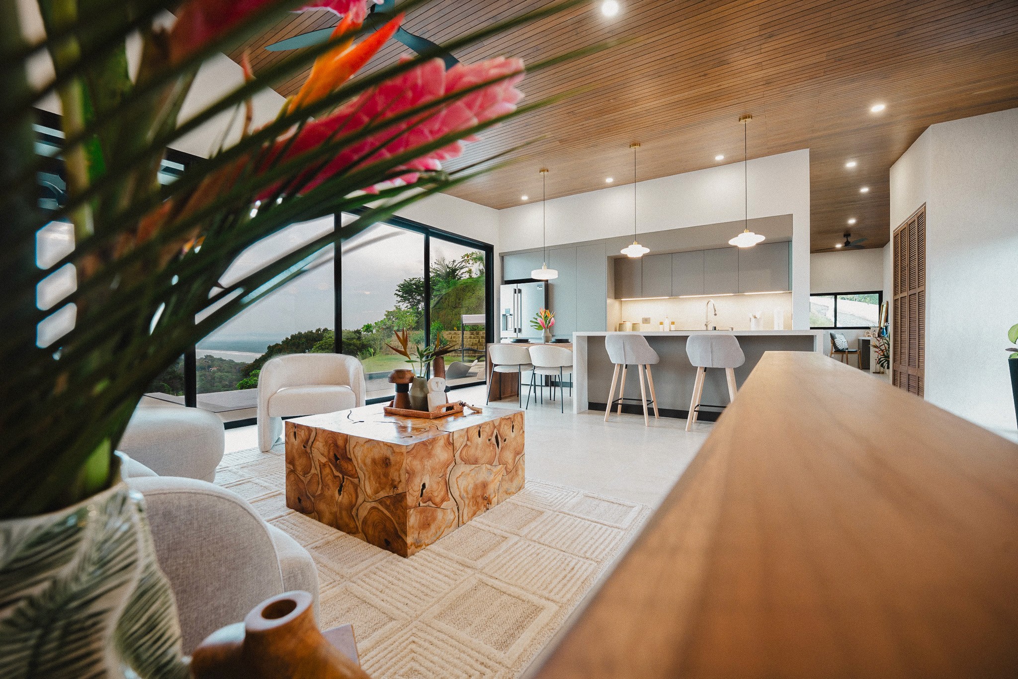 View from patio into the suite, surrounded by lush greenery, queen bed framed inside with neutral-toned decor.
