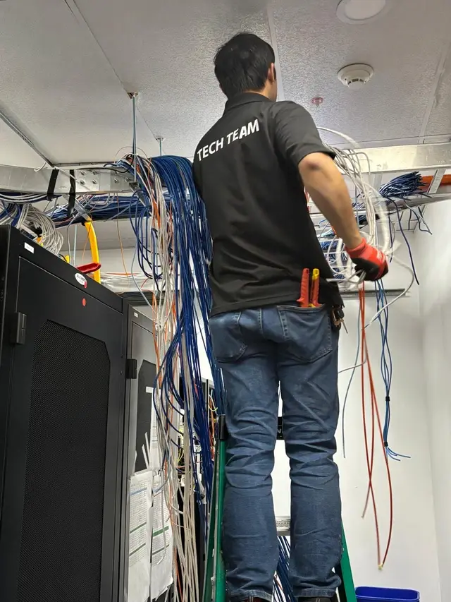 Technician pulling low-voltage network cables from walls and ceiling during structured cabling removal in a server room