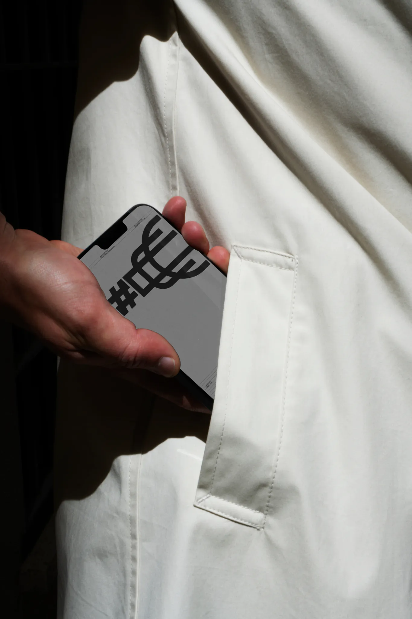 Hand holding an iPhone with a minimal black and white interface, partially in the pocket of a white coat, emphasizing clean design.