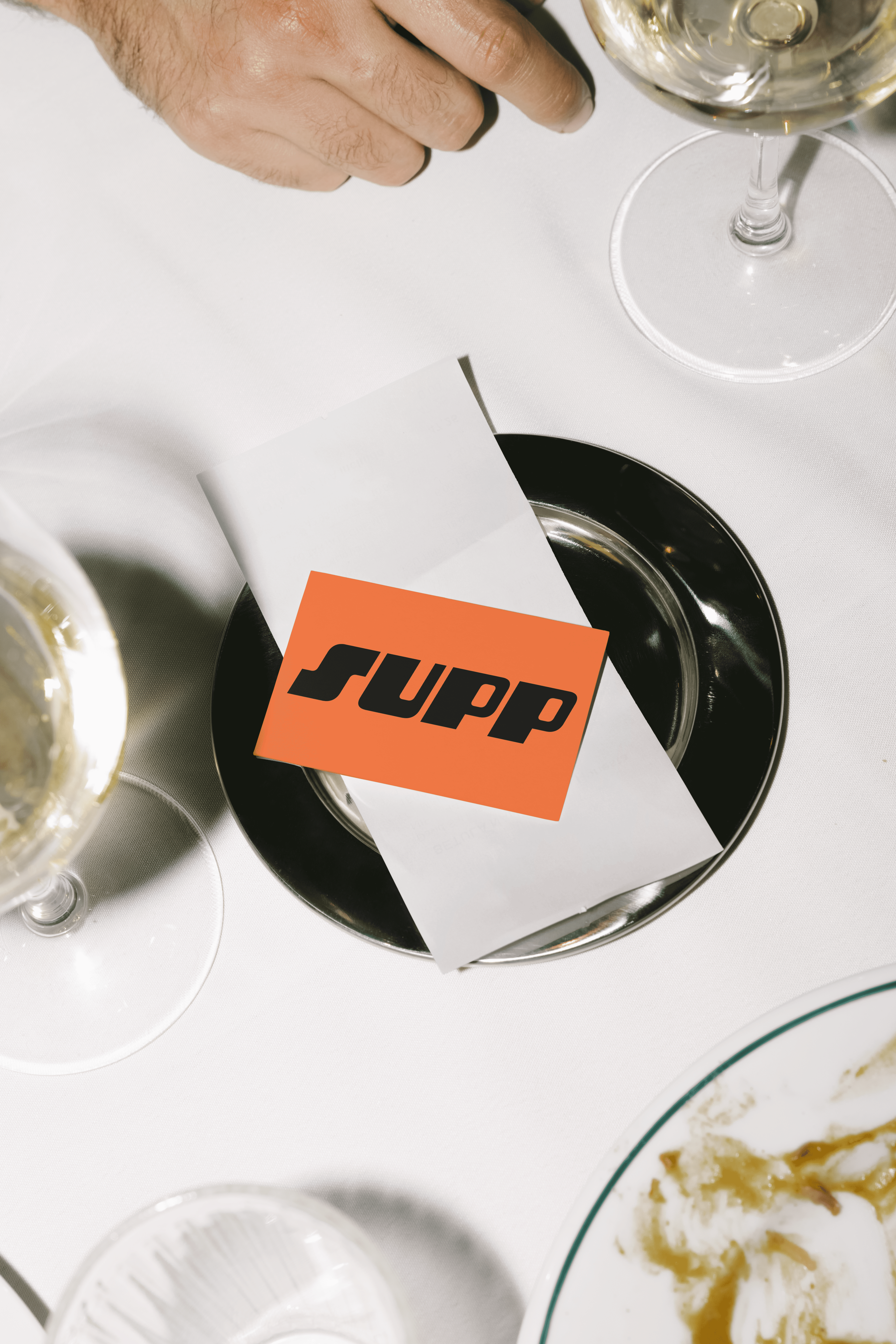 A Supp branded card on a restaurant place setting with wine glasses