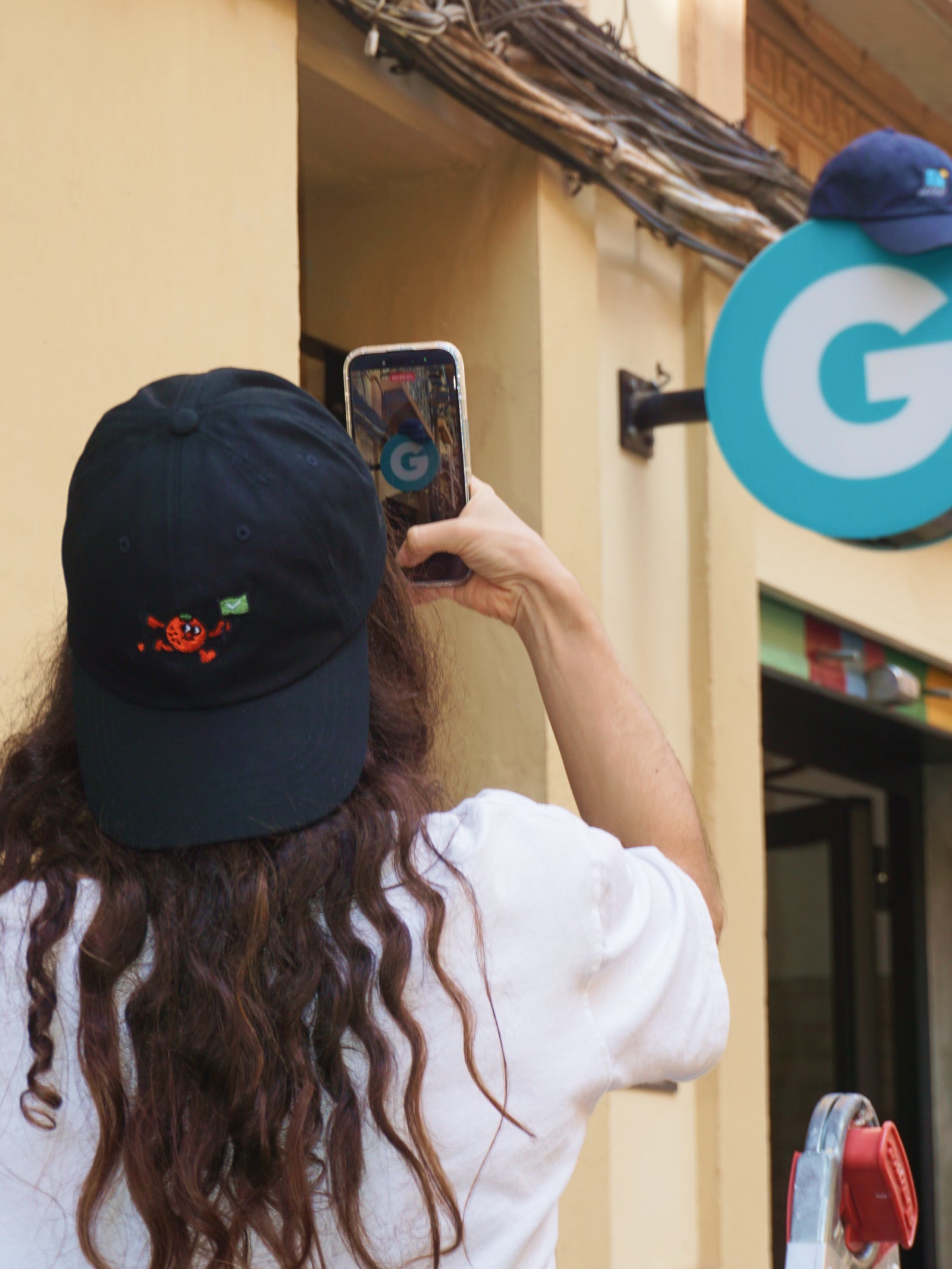 Person taking a photo of a store sign with a phone, wearing a black cap with a logo.