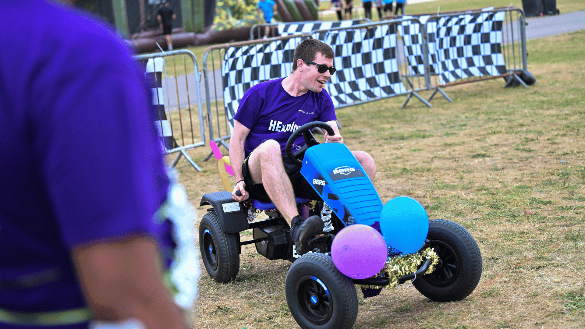 Outdoor team-building event with participants wearing matching blue shirts, taking part in inflatable obstacle courses and games, smiling and cheering, with the words 'ENTER A TEAM' in large bold white and green text across the image.