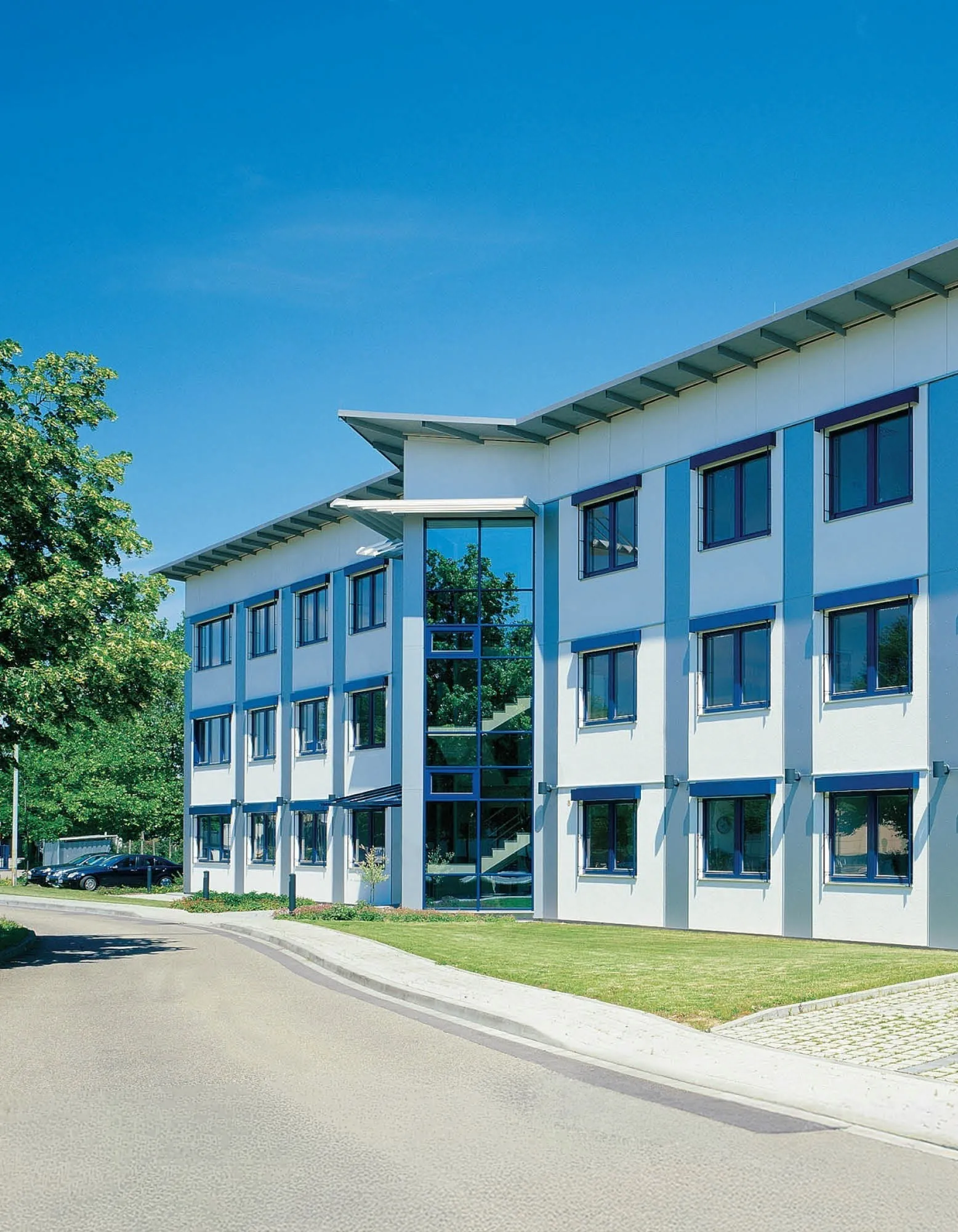 Moderne Bürogebäude-Fassade mit blauen Fenstern und einem Glas-Atrium unter einem strahlend blauen Himmel.