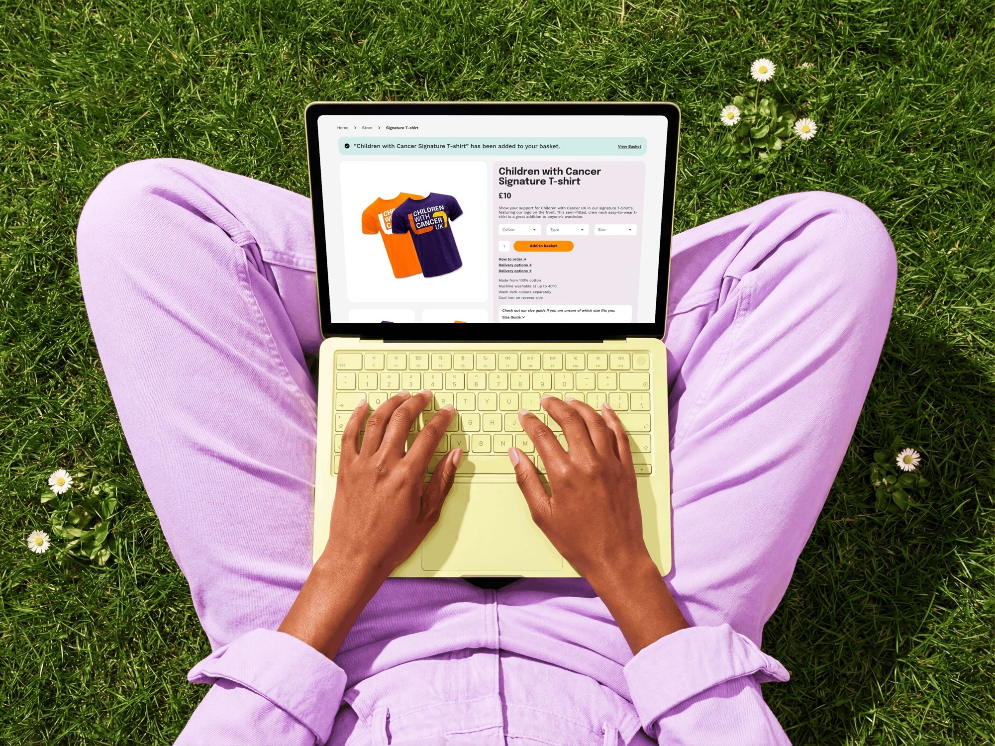Shop product page on a laptop, showing a Children with Cancer UK t-shirt with size options and an add to basket button