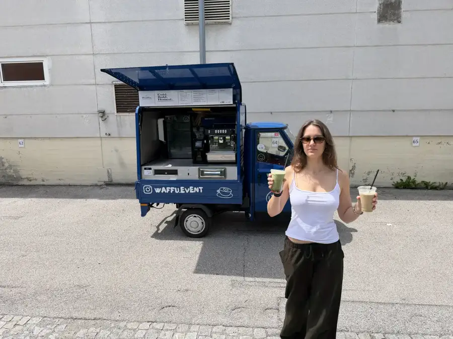 Gast mit zwei Kaffeegetränken vor der blauen WAFFU Ape