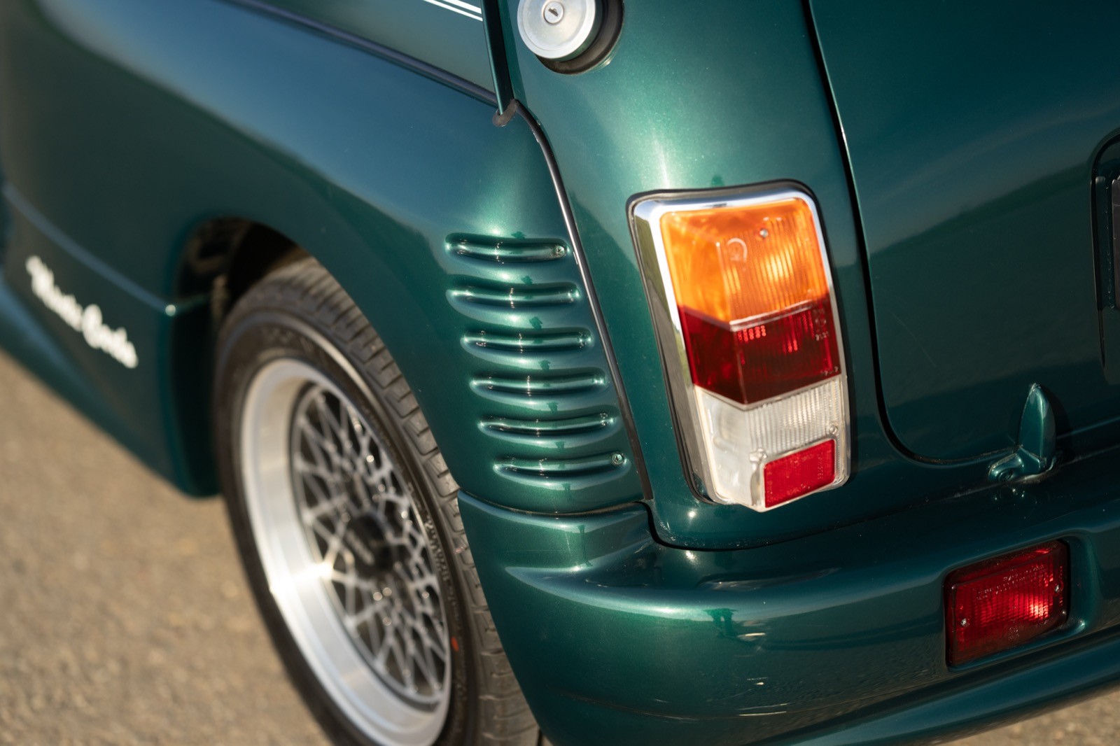 Close-up of a green car's rear, showing the tail light and textured fender area.