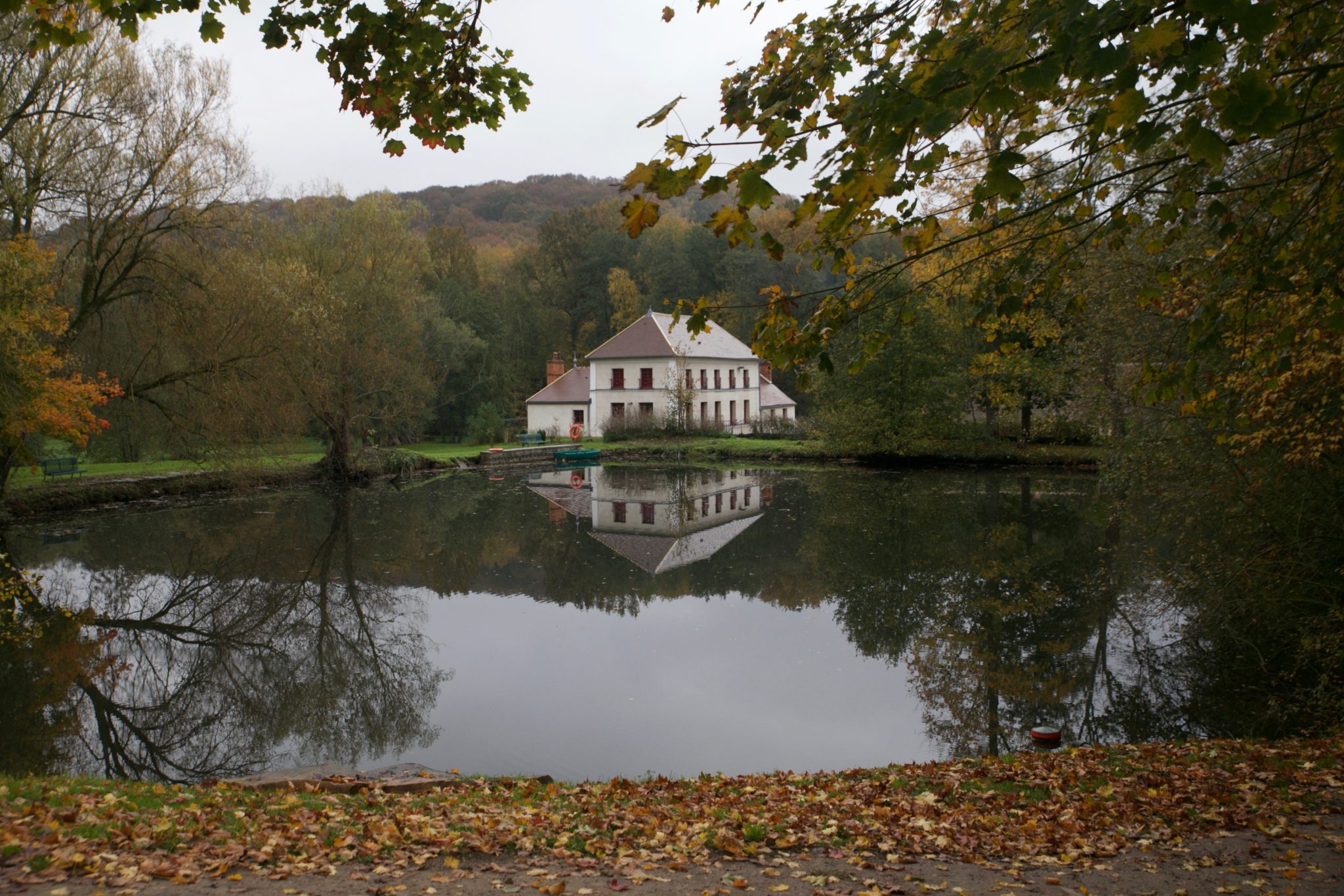 White country manor house reflected in a still pond, framed by autumn foliage