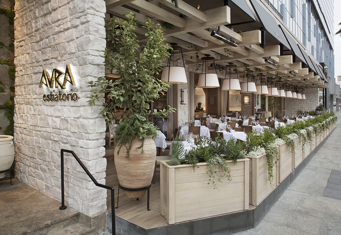 Exterior view of a modern restaurant with greenery, comfortable seating, and a welcoming atmosphere.