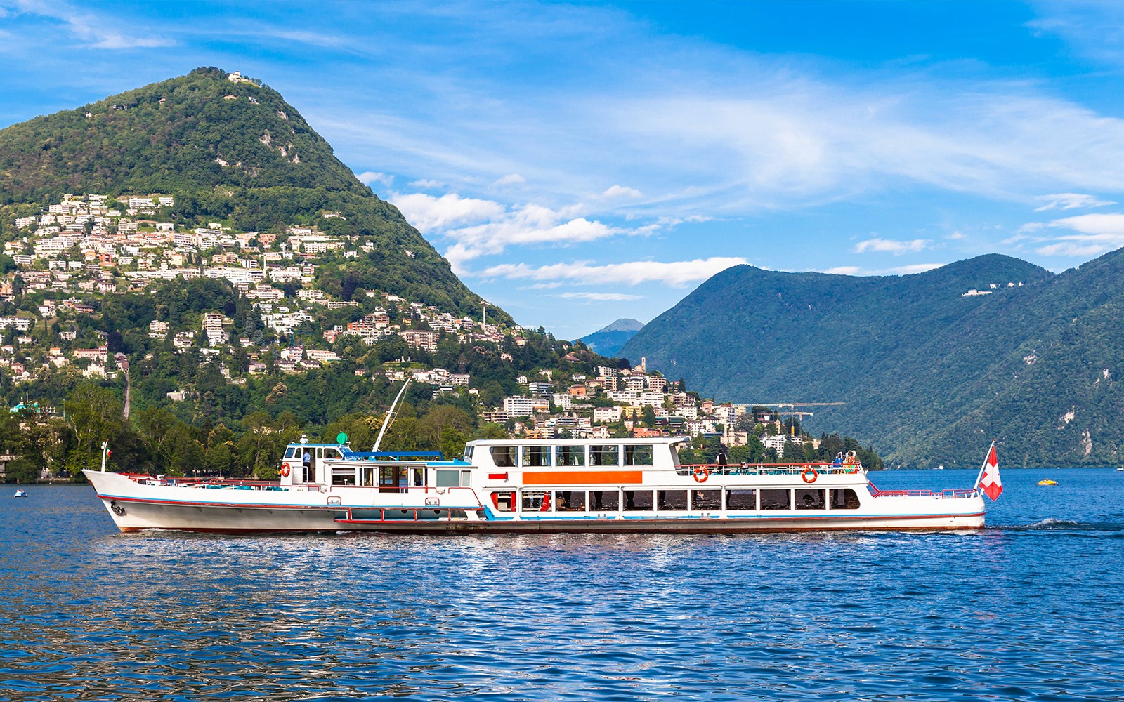 Cruise boat on Lake Lugano with hillside town and mountains in the background.