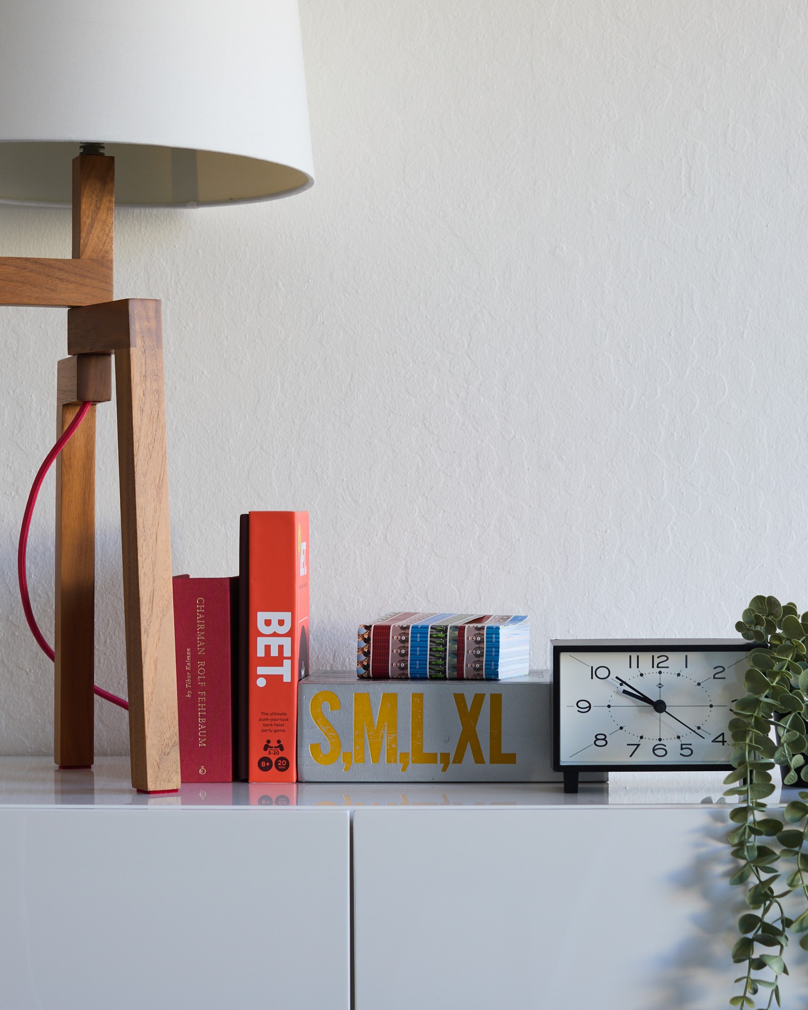 BET. game box standing on a shelf between design books, next to a wooden lamp and clock, showing the spine with the BET. logo.