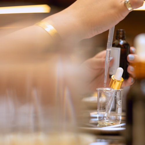 Isang tao na maingat na naghahalo ng mga sangkap ng pabango gamit ang dropper at beaker sa isang interactive na workshop.