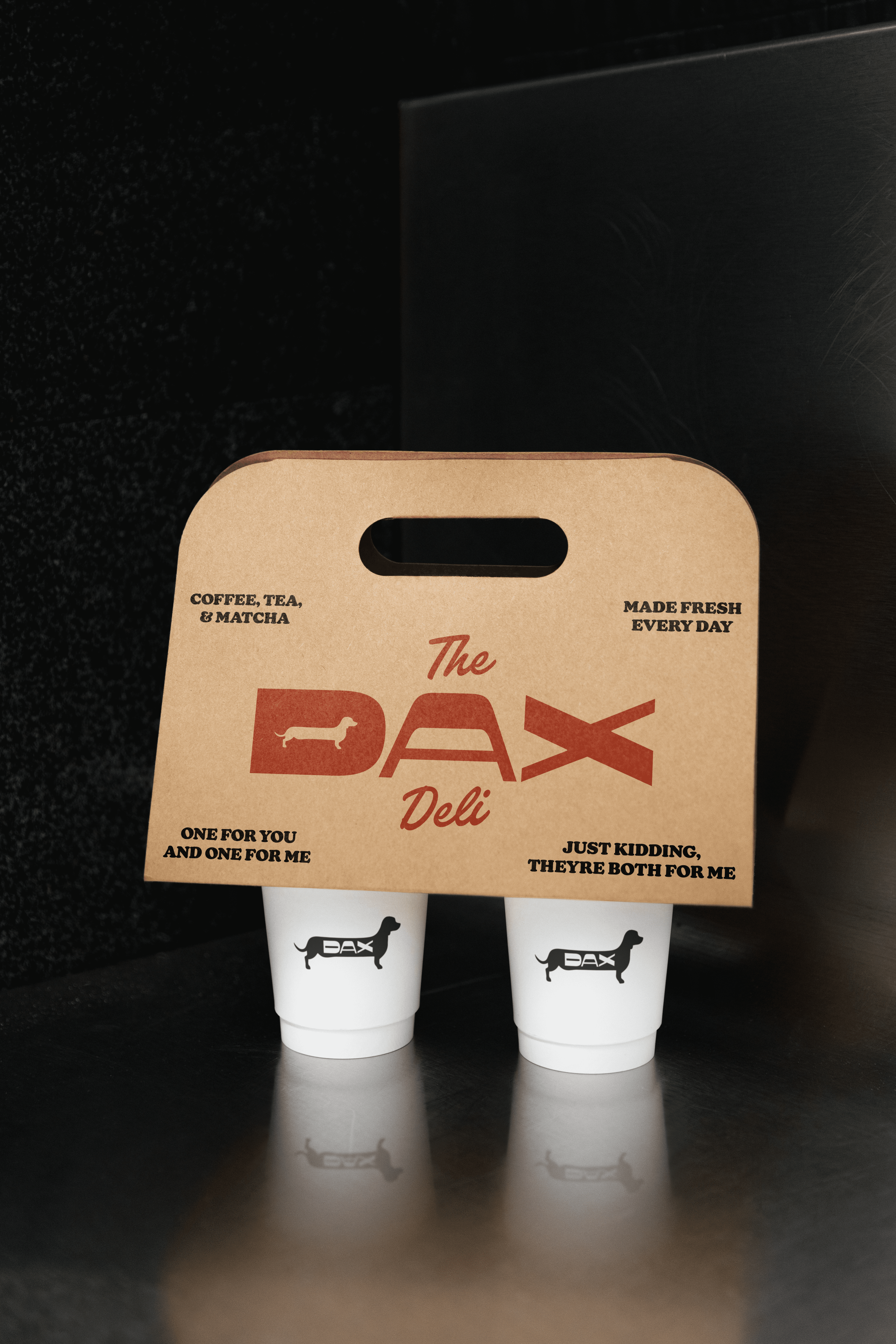 A coffee cup holder branded with The Dax Deli logo