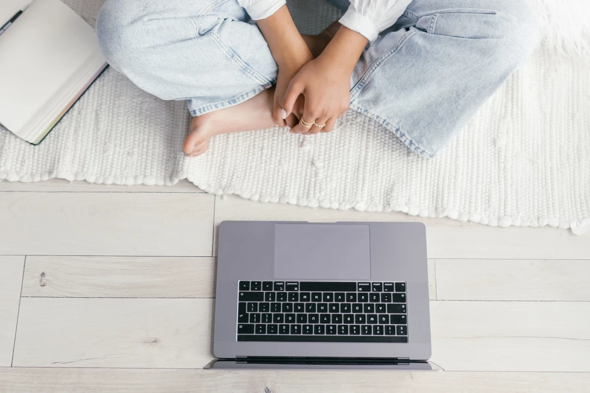 Person sitting cross-legged on a bed with an open laptop, preparing for an online therapy session.