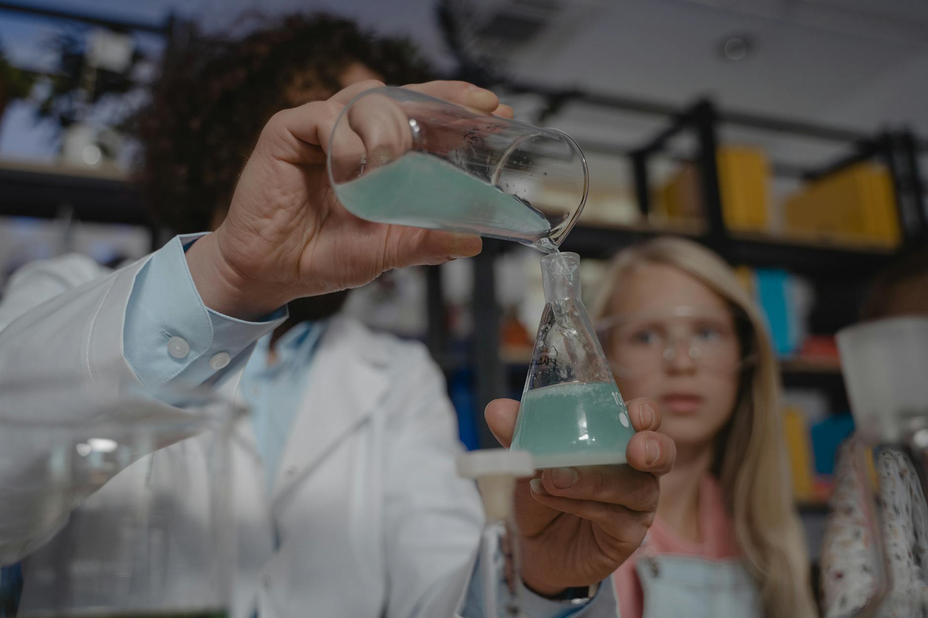 A high school science instructor demonstrates a chemical reaction using colorful liquids in beakers for a small group.