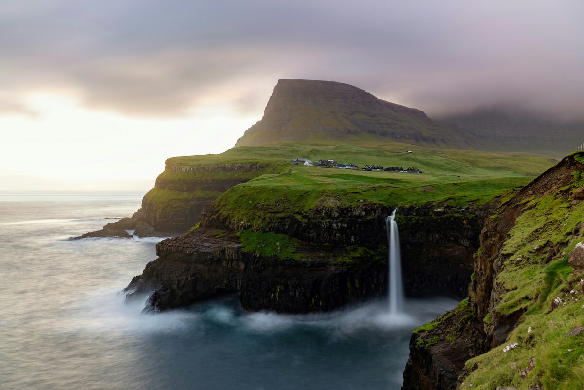 Gasadalur waterfall dropping into the ocean with green cliffs Faroe Islands