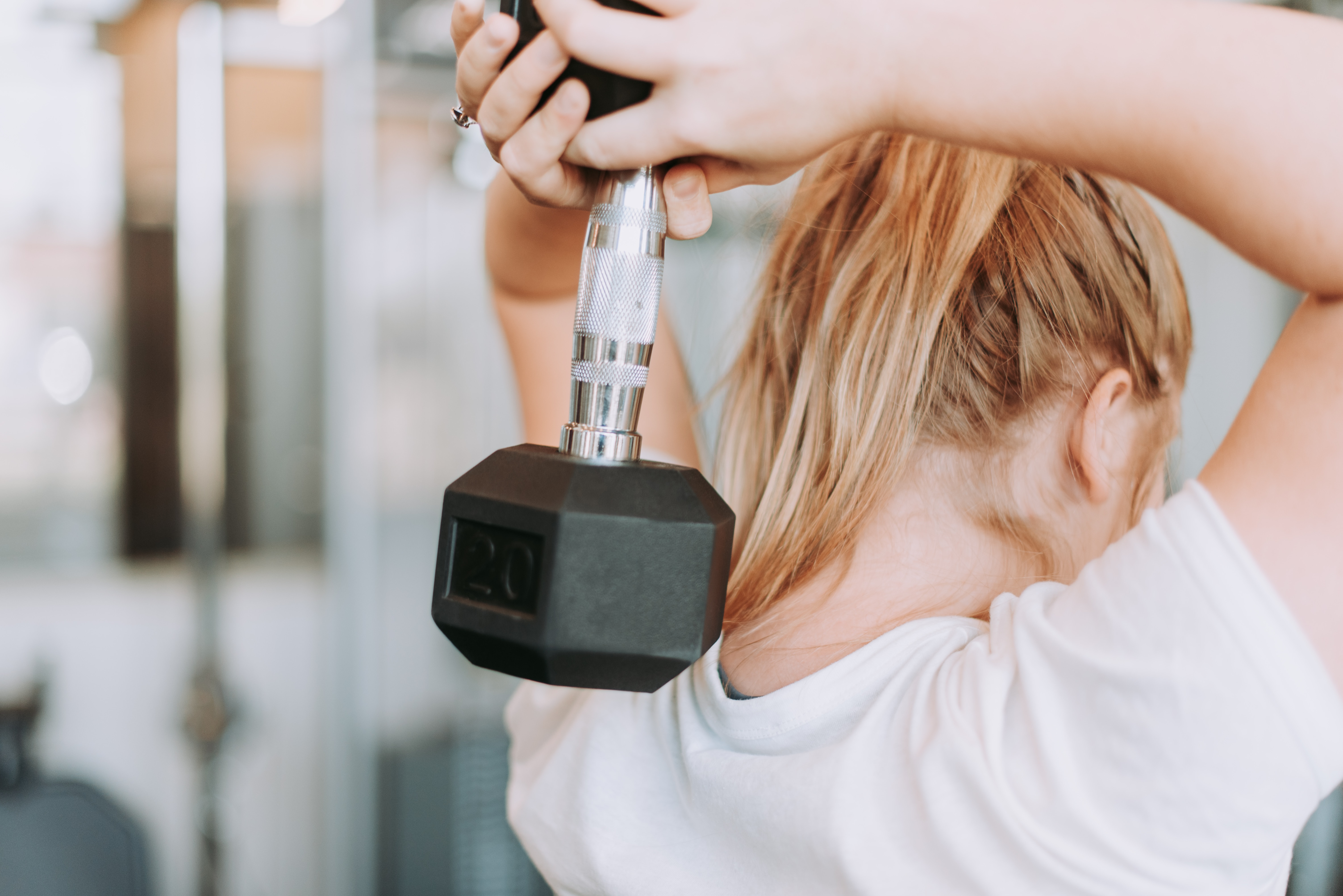 Woman performing overhead triceps extension with a 20-pound dumbbell, focusing on upper body strength, muscle control, and safe resistance training form.