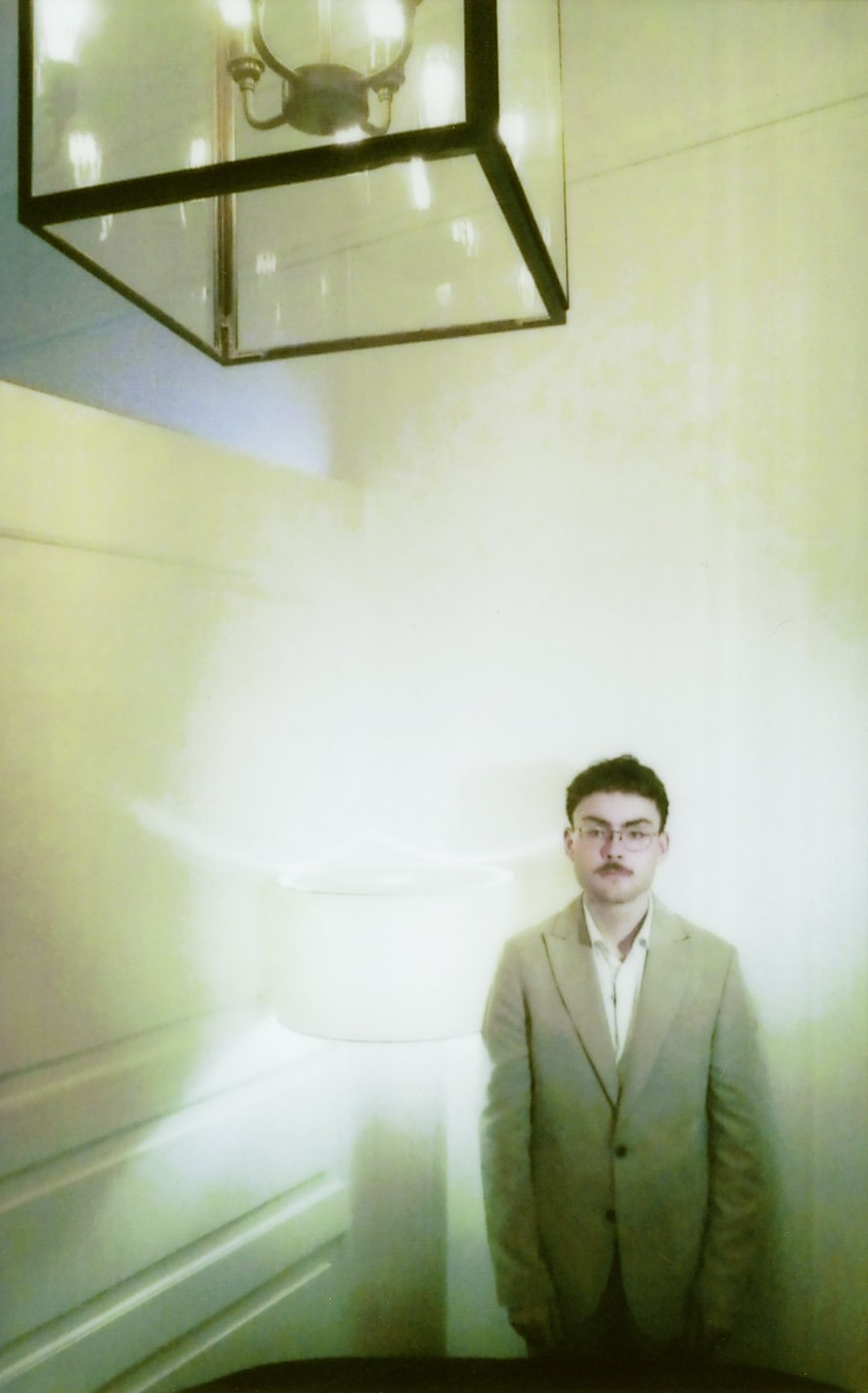 Jonathan Miehlich, Head of Production standing in a corner, tucked behind a couch next to a light, looking unimpressed