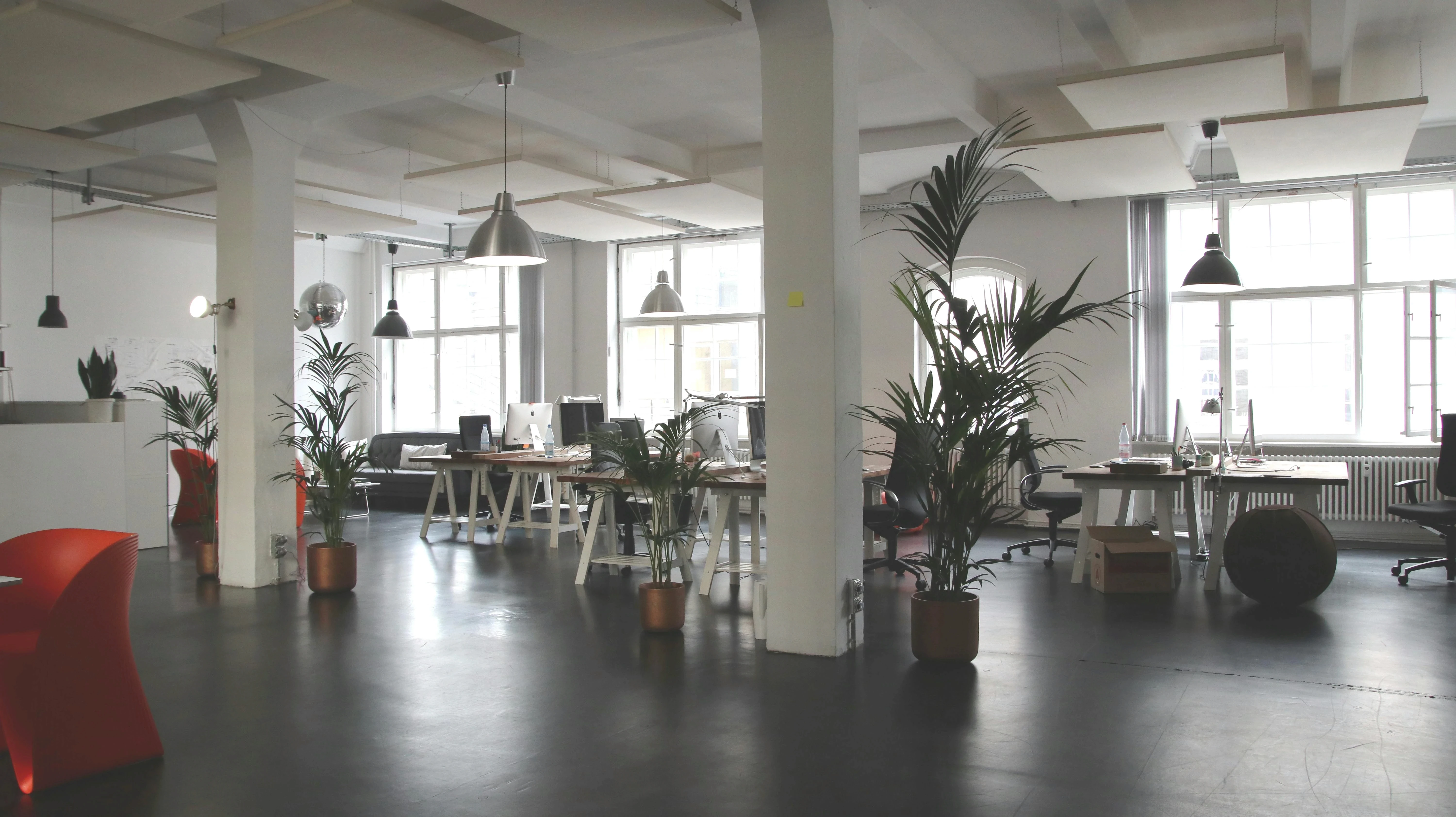 High-ceilinged industrial loft workspace with white pillars, desks, and open floor plan.