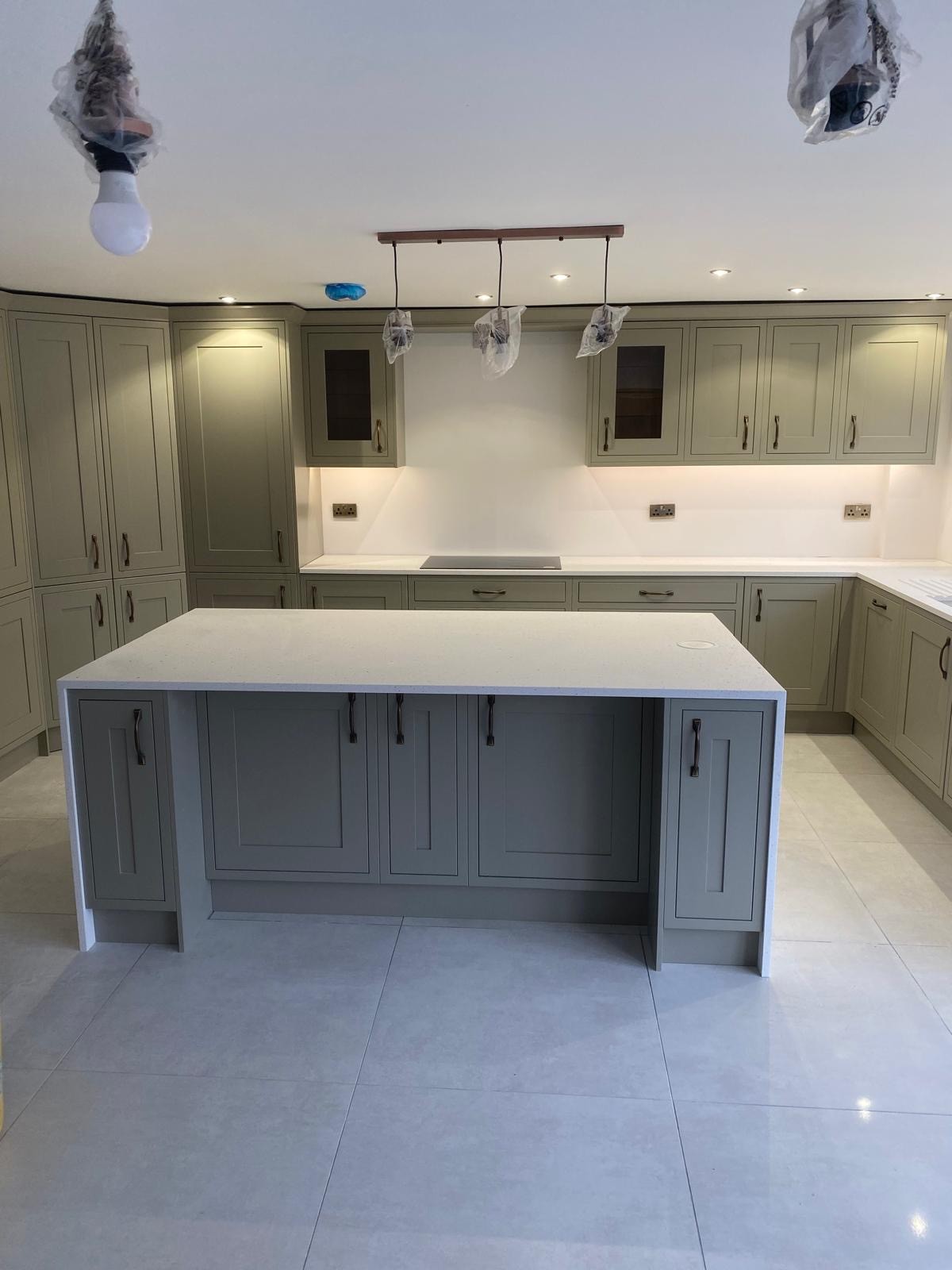 Bespoke kitchen renovation by PPM Builders in Northampton featuring sage green shaker cabinets, a quartz island worktop, and modern under-cabinet lighting for a stylish and functional space.