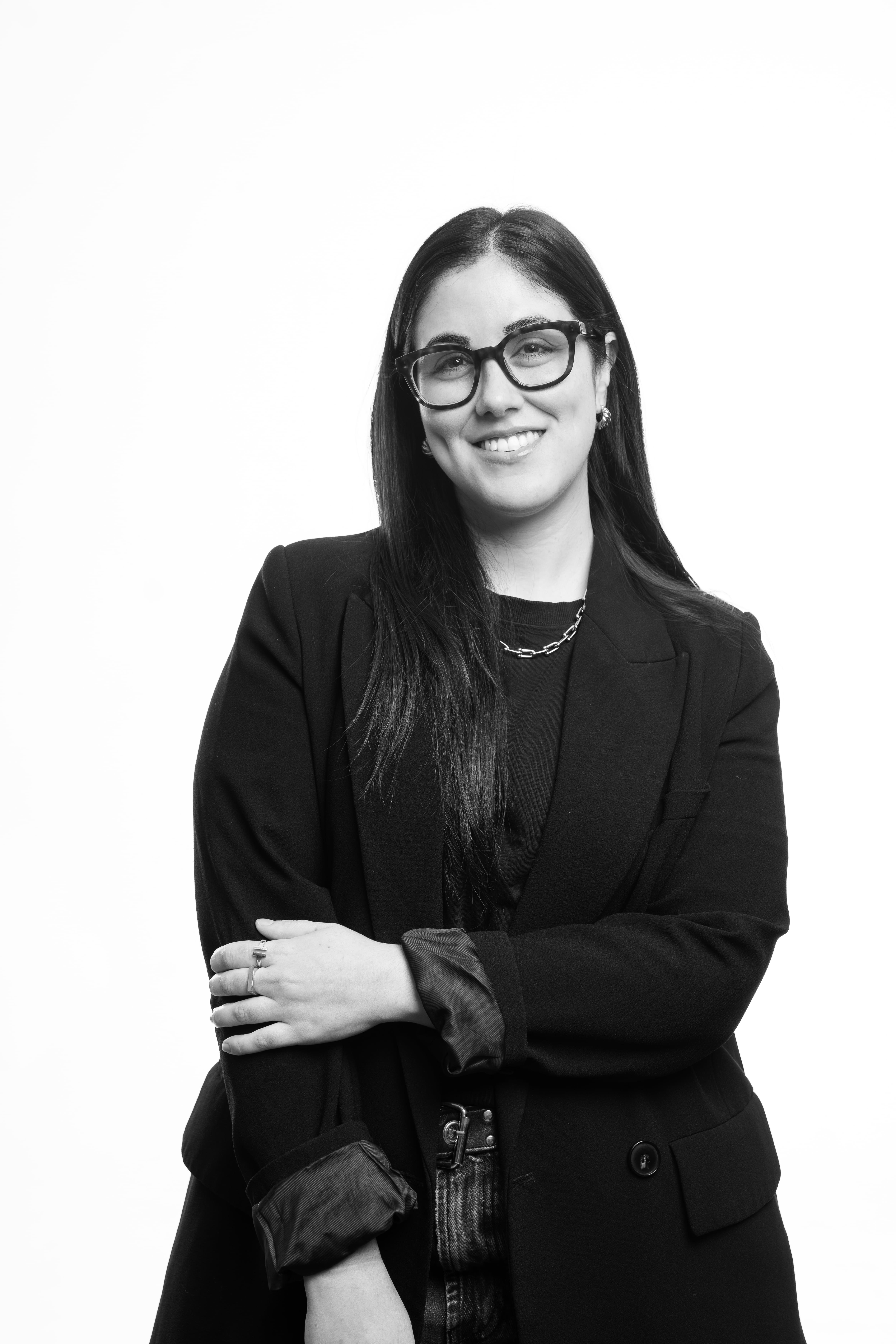 A black and white portrait of a smiling individual wearing glasses and a dark blazer, exuding a confident and friendly demeanor.