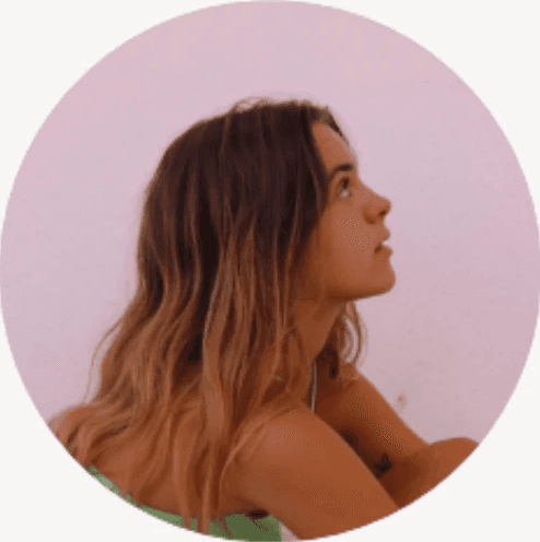 Young woman with curly hair, glasses, and an orange sweater smiling.