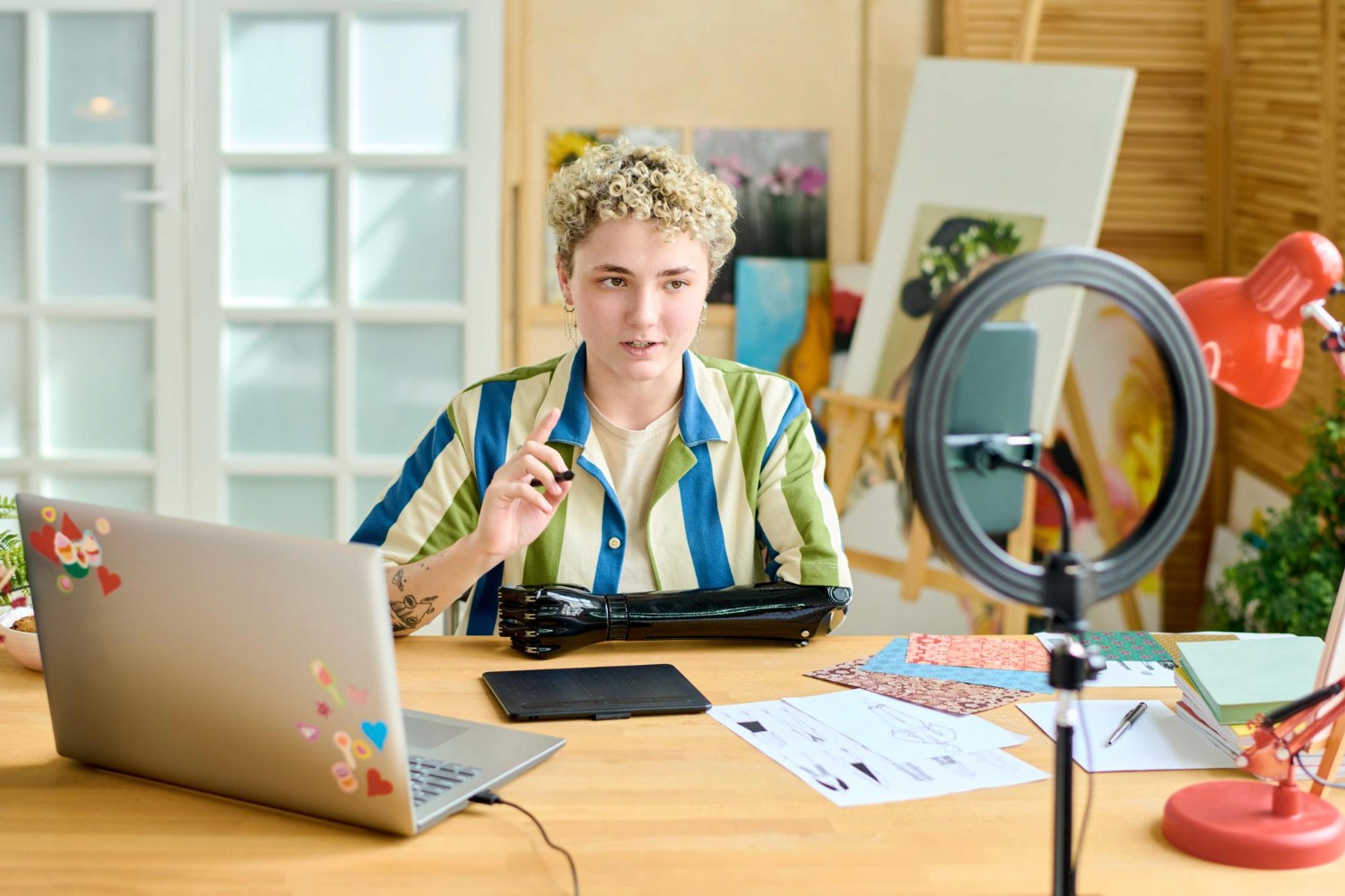 A woman seated at a desk, working on a laptop with a camera positioned nearby, focused on her tasks.