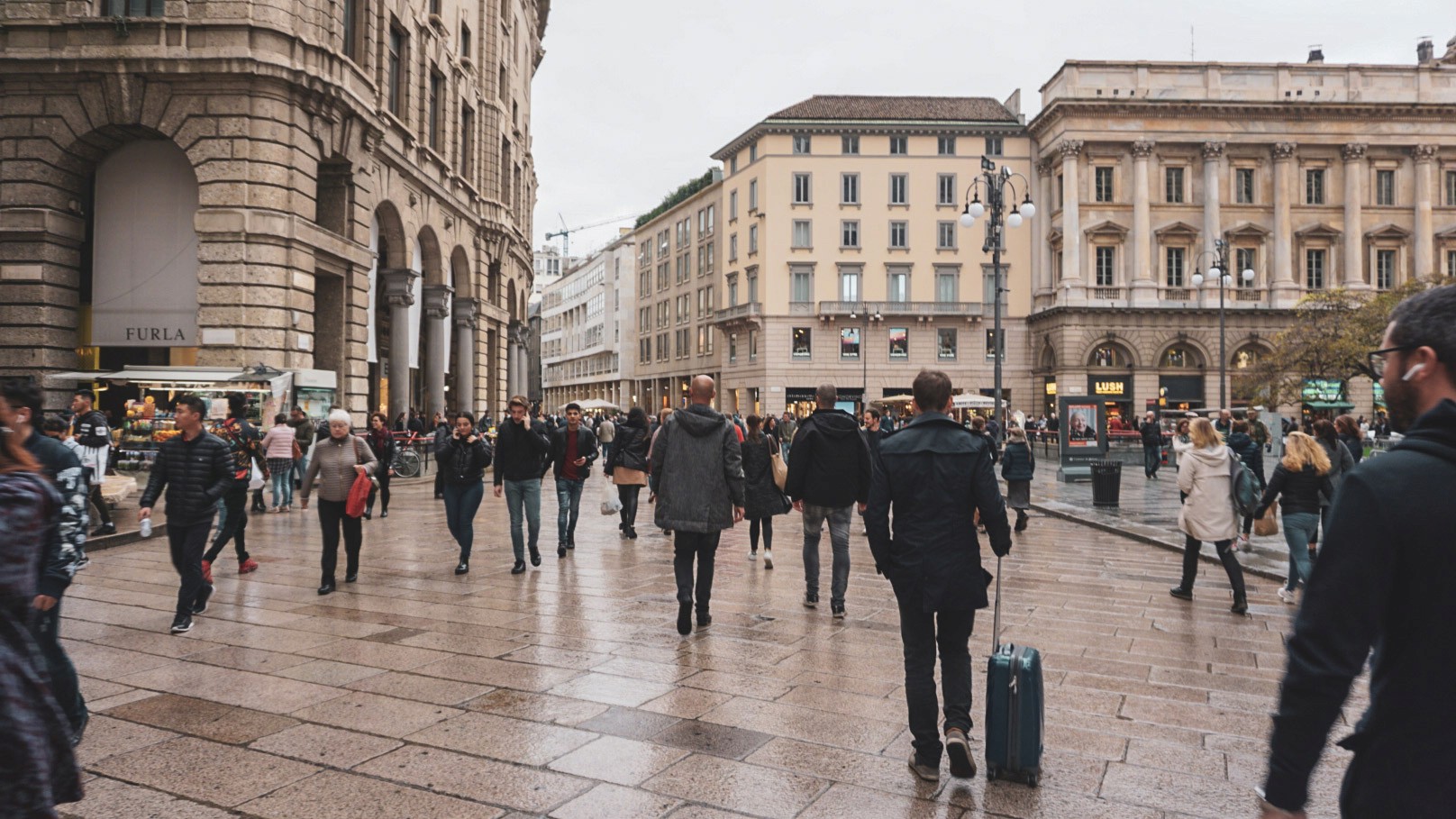 Lively Milan street scene with crowds walking across a stone square surrounded by classical buildings, photographed by Janice Chen.