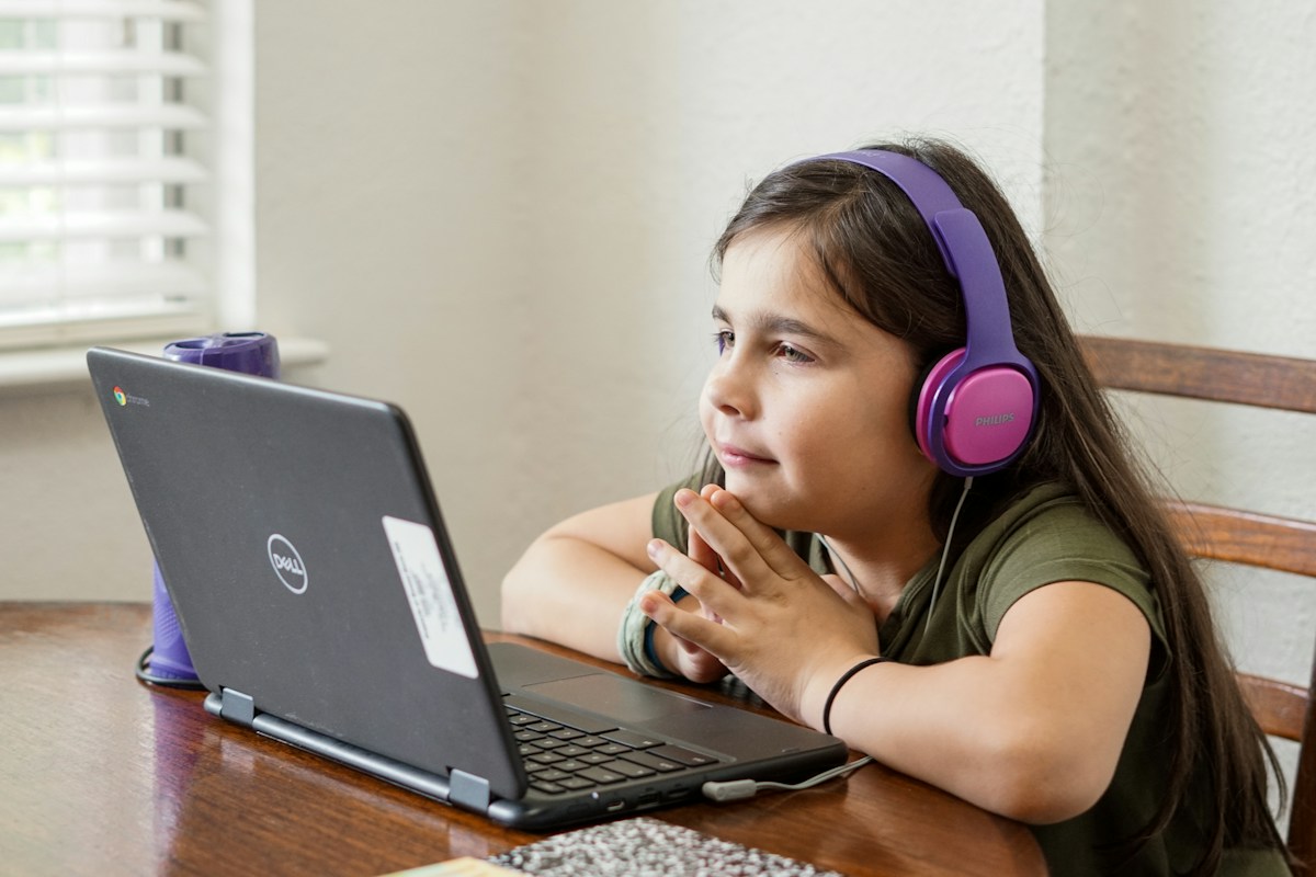 A girl in headphones smiling at a laptop during an online lesson