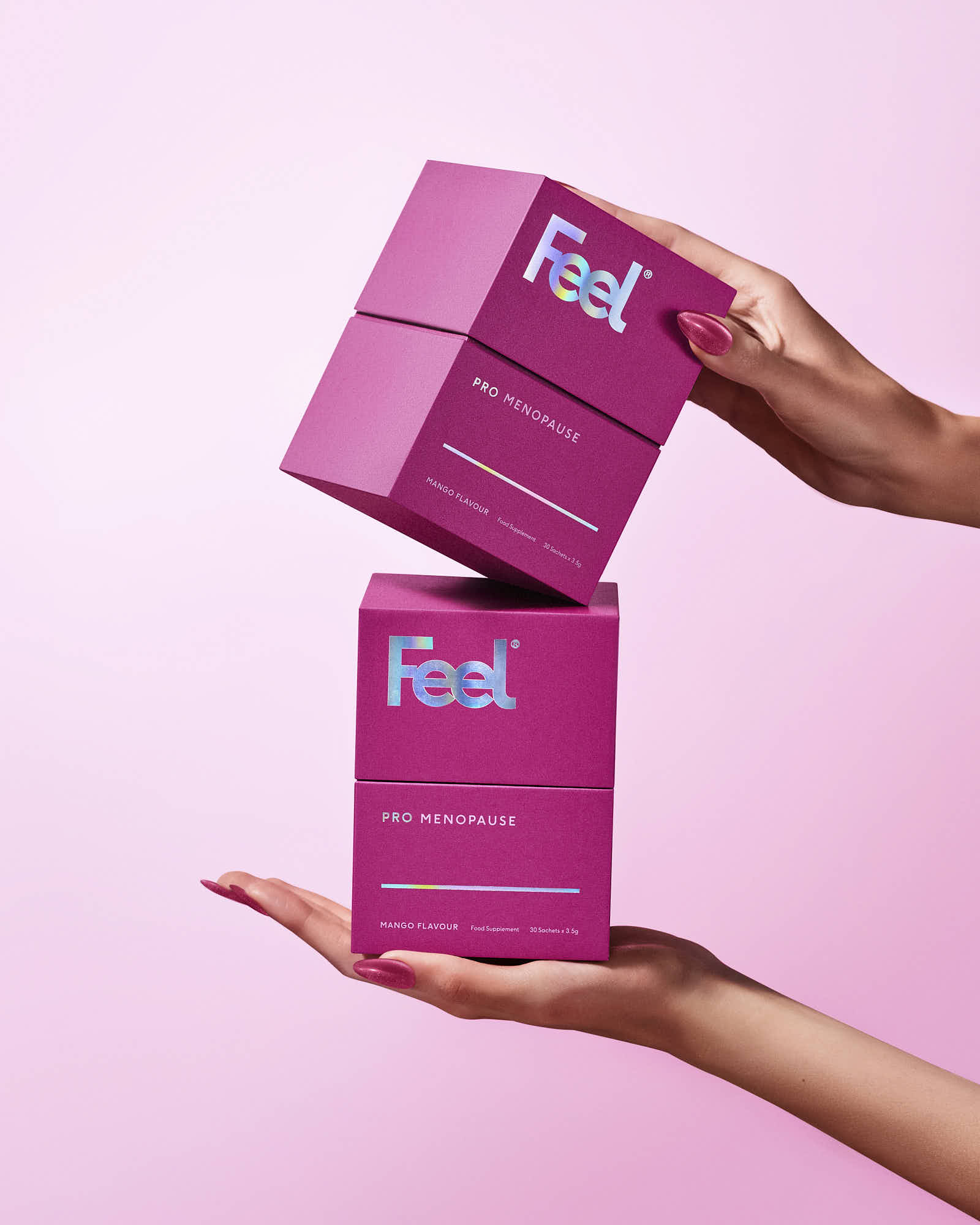 Two pink boxes are stacked on top of each other, held by hands against a soft pink background.