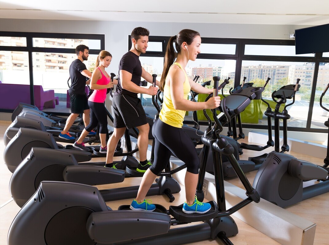 group of friends at a sunny gym with lots of natural light doing an elliptical weight loss routine together