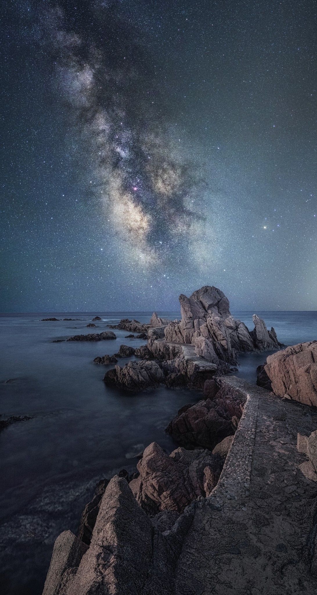 Rocks jutting into a body of water with the milky way in the sky