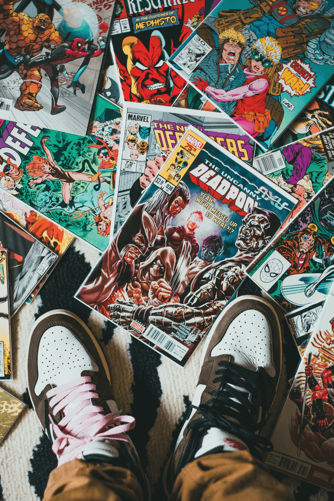 A bunch of comic books on the floor and someones feet with nike shoes that have pink laces