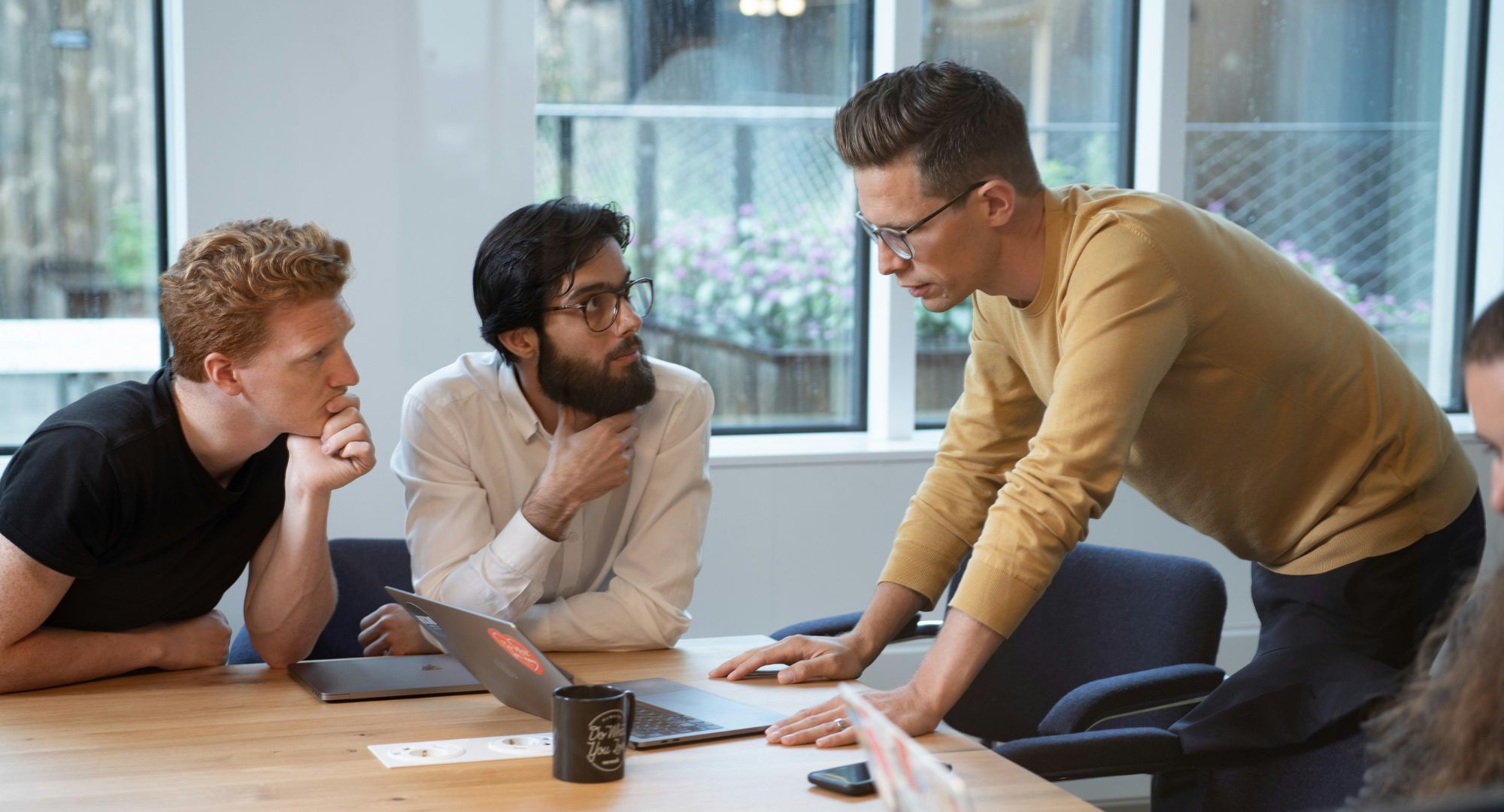 três homens numa reunião em torno de uma mesa de madeira com notebooks