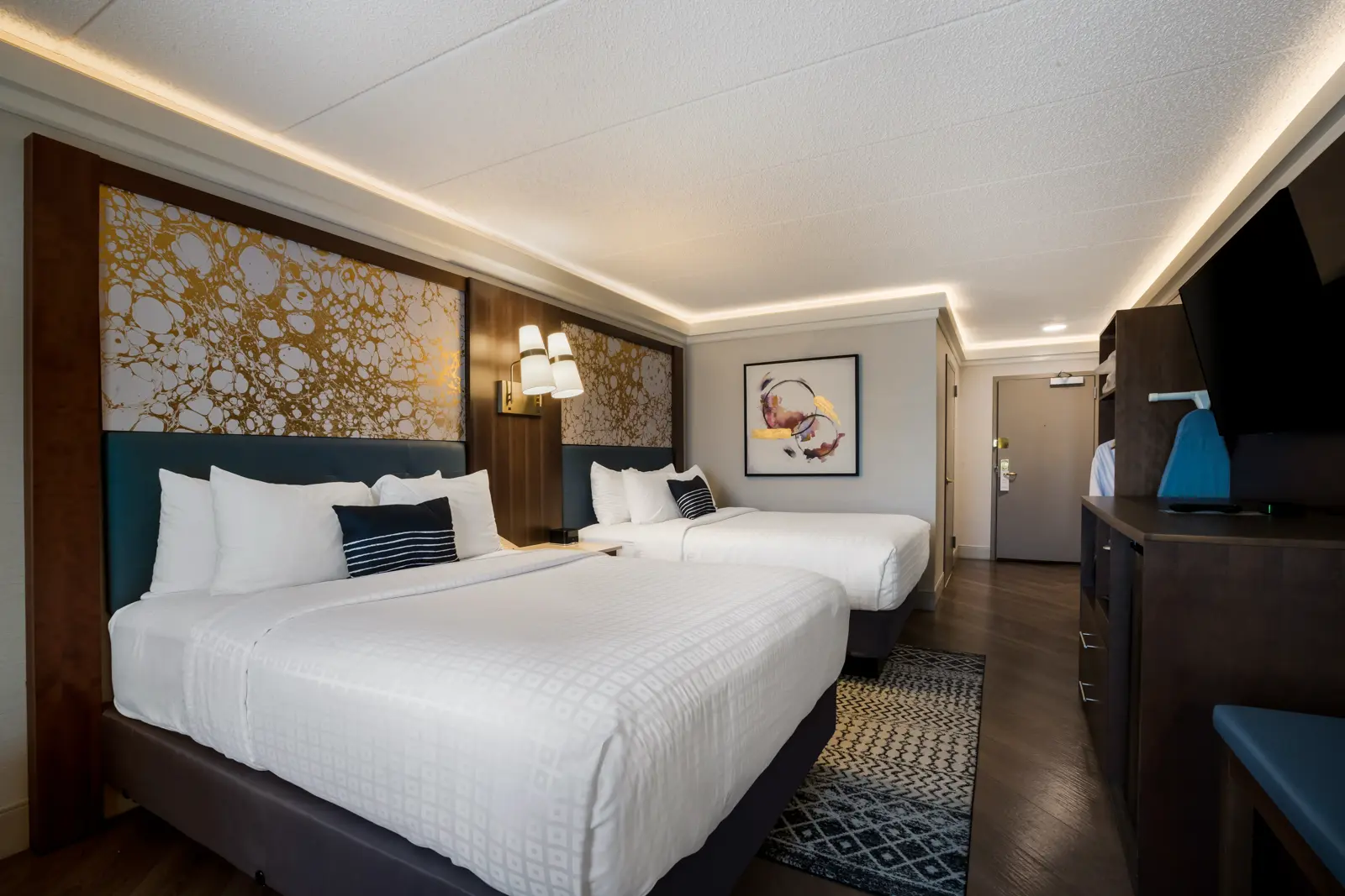 Bright modern hotel room with two beds and a desk.