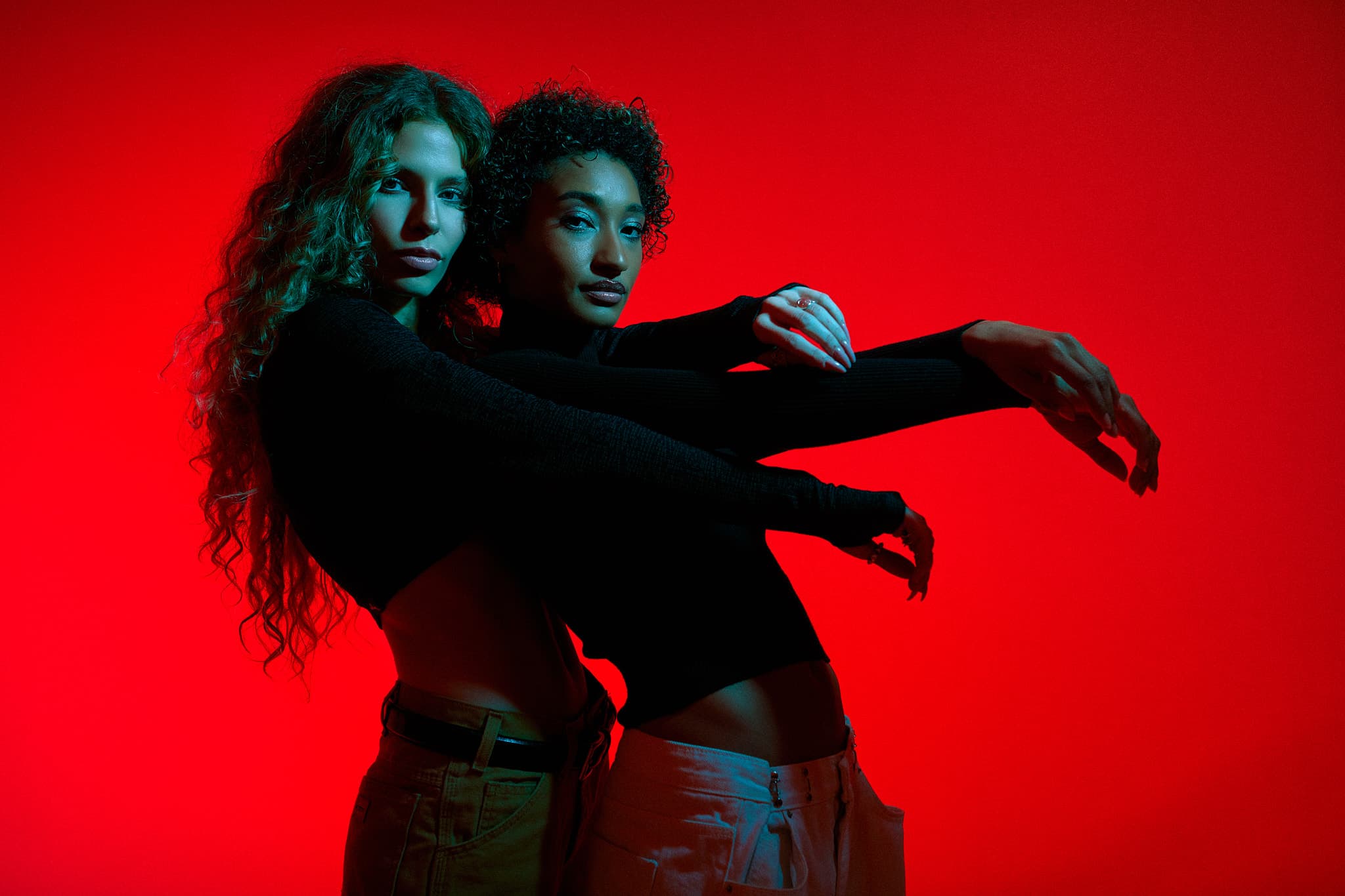 Two models pose together in front of a vibrant red background, photographed in a Shreveport studio.