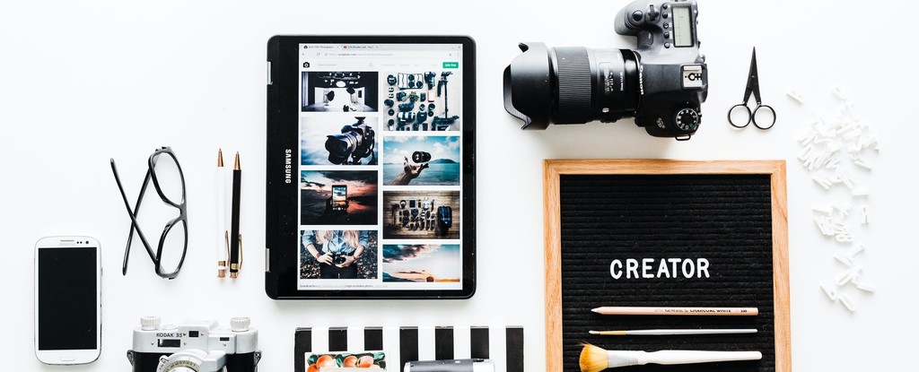 Photography equipment and tablet display on white desk showcasing creative workspace setup.