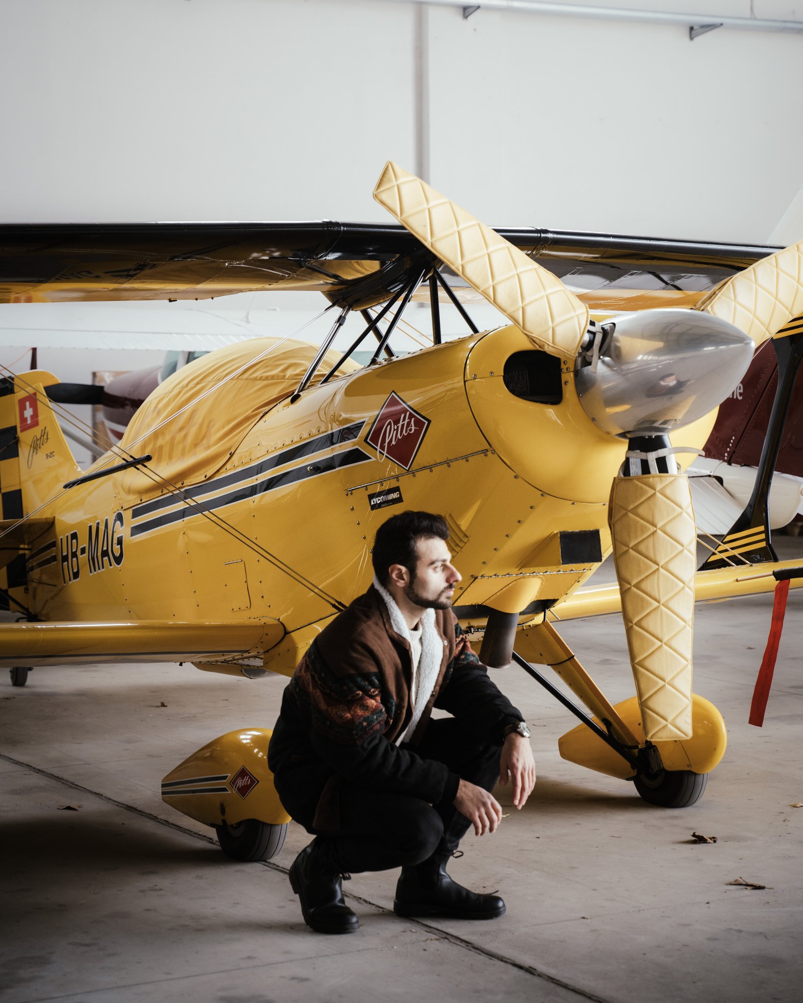 A person squats beside a vintage yellow airplane inside a hangar, showcasing aviation nostalgia.
