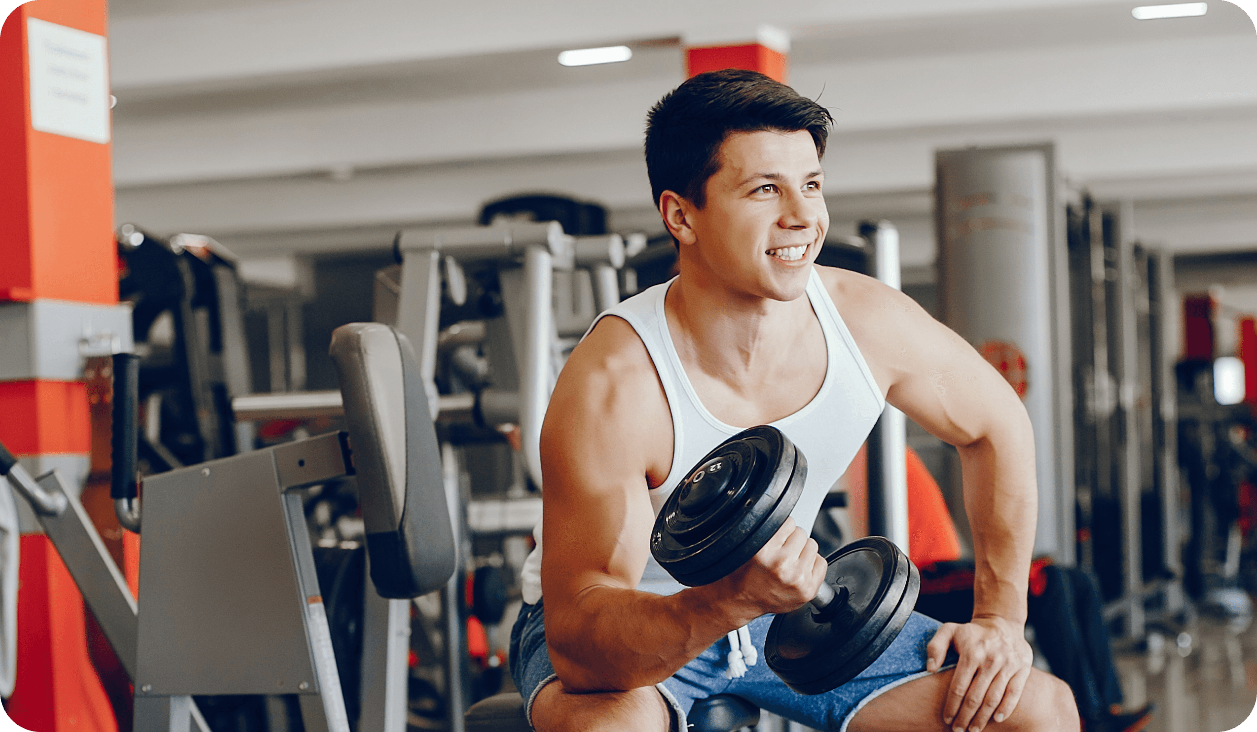 Smiling man doing a dumbbell curl in a gym.