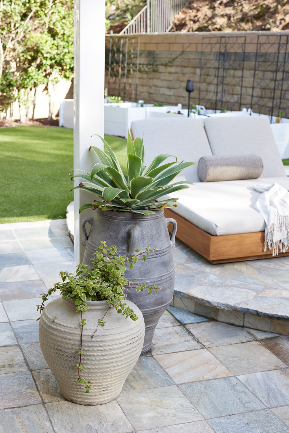 This serene outdoor space features lush greenery, earthy tones, and sun beds with linen upholstery for a perfect relaxation area